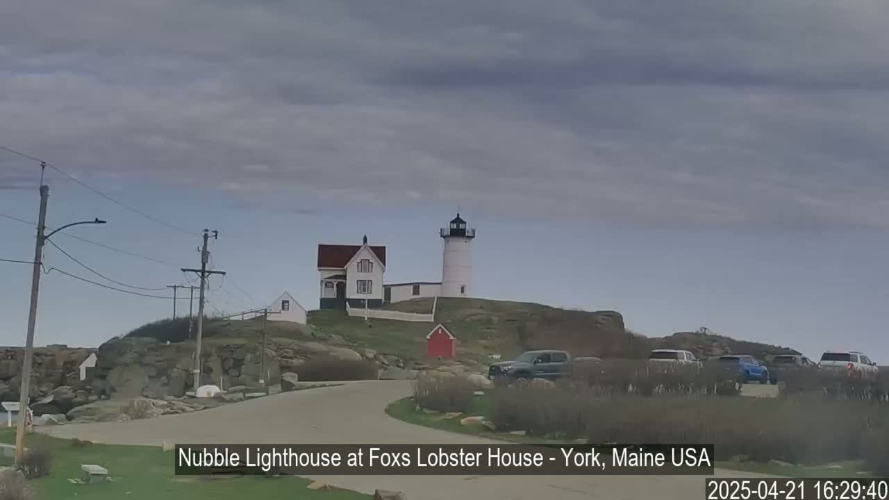 A white lighthouse sits atop a rocky outcrop, with a smaller building nearby, under an overcast sky.