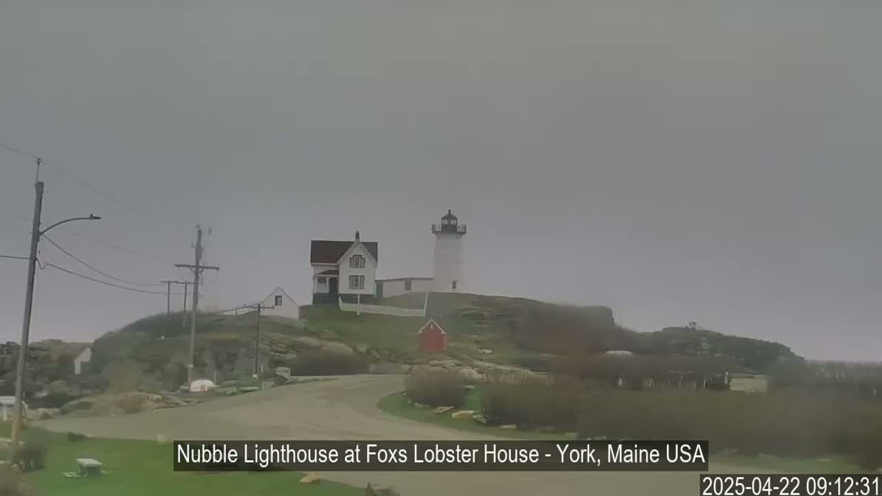A lighthouse and accompanying buildings sit atop a rocky hill on an overcast day.