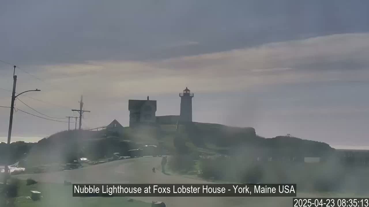 A lighthouse and other buildings sit atop a hill on an overcast day with a hazy atmosphere.