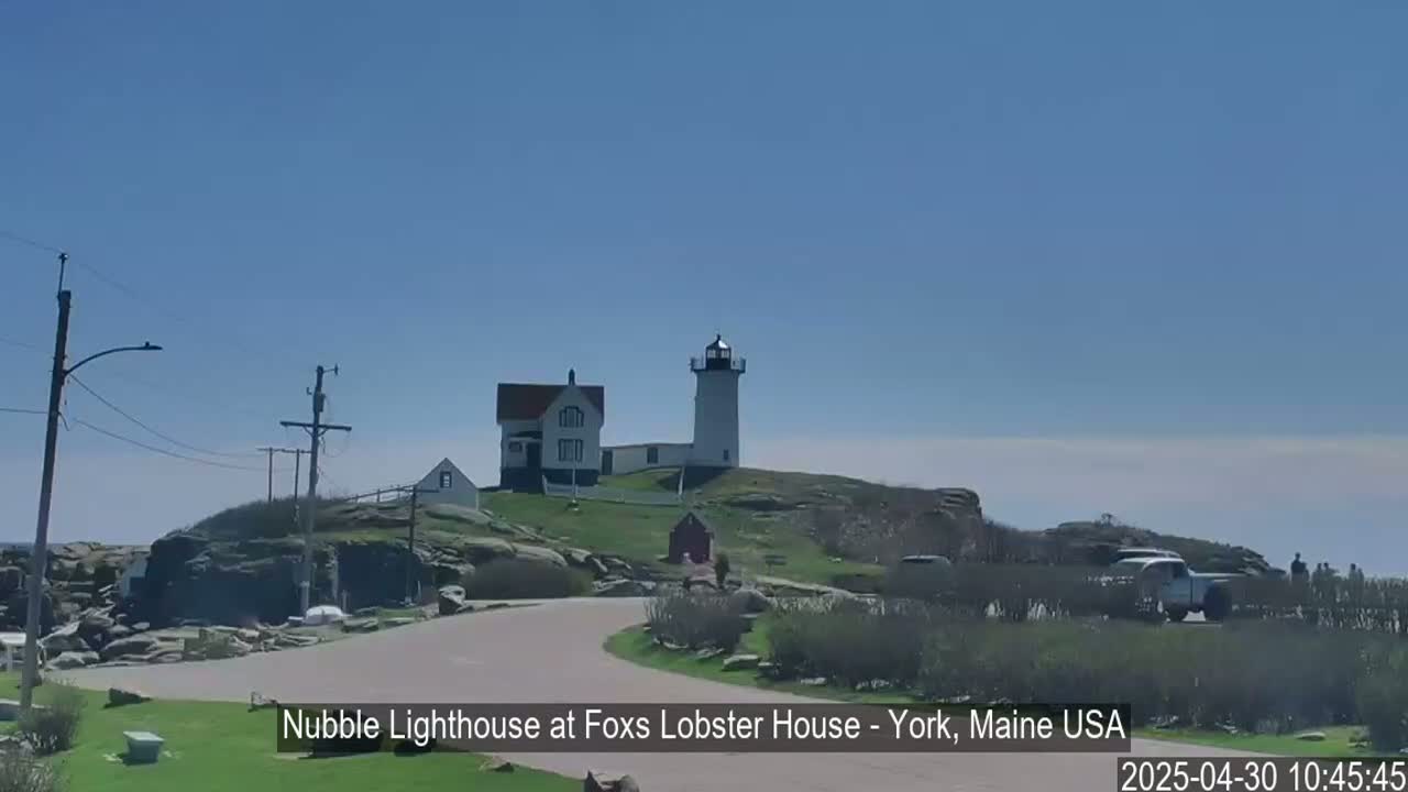 A lighthouse and keeper's house sit atop a rocky outcrop on a sunny day.