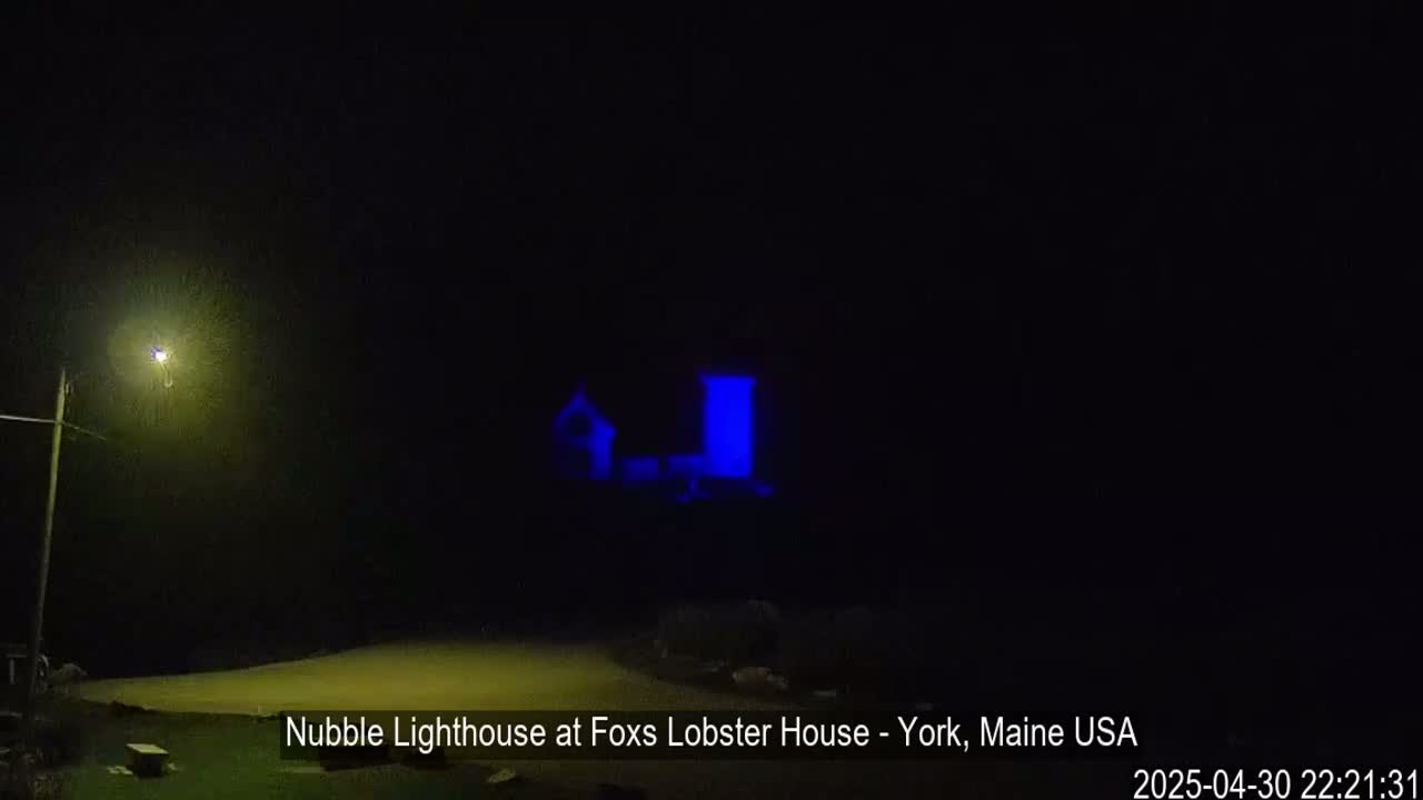A dimly lit lighthouse is visible at night under a dark sky.