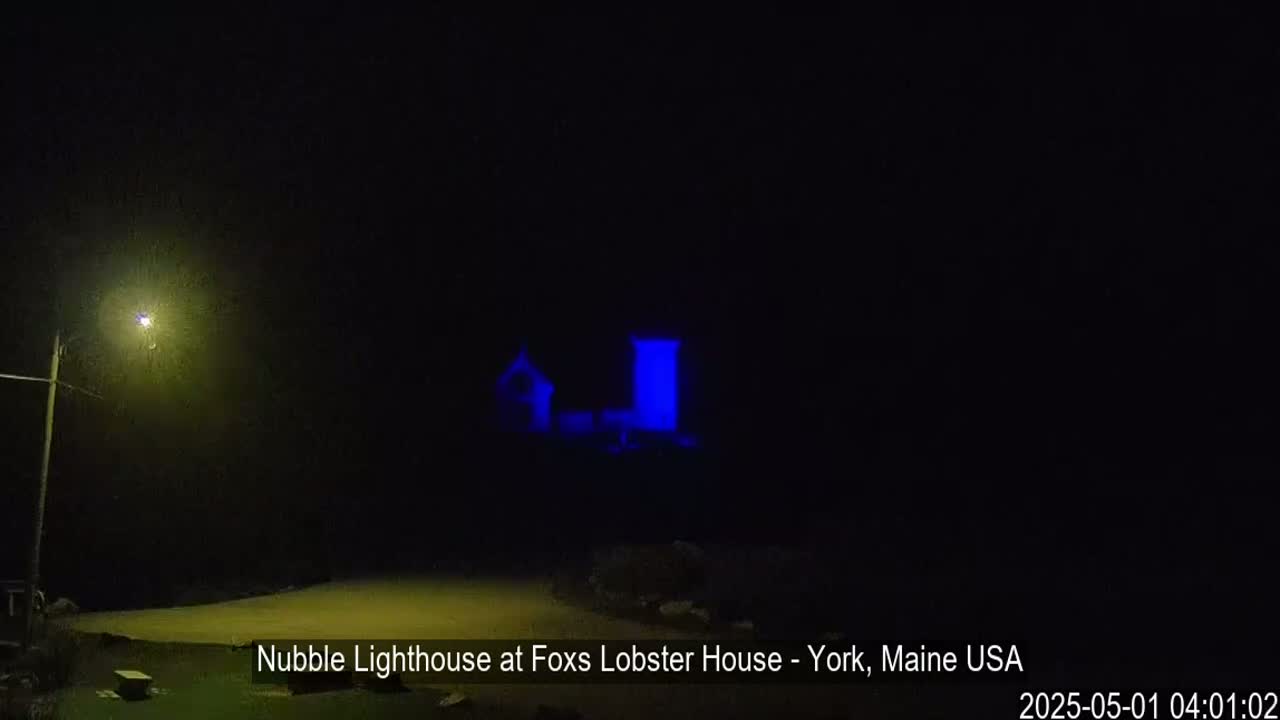 A lighthouse, illuminated in blue, is visible at night.