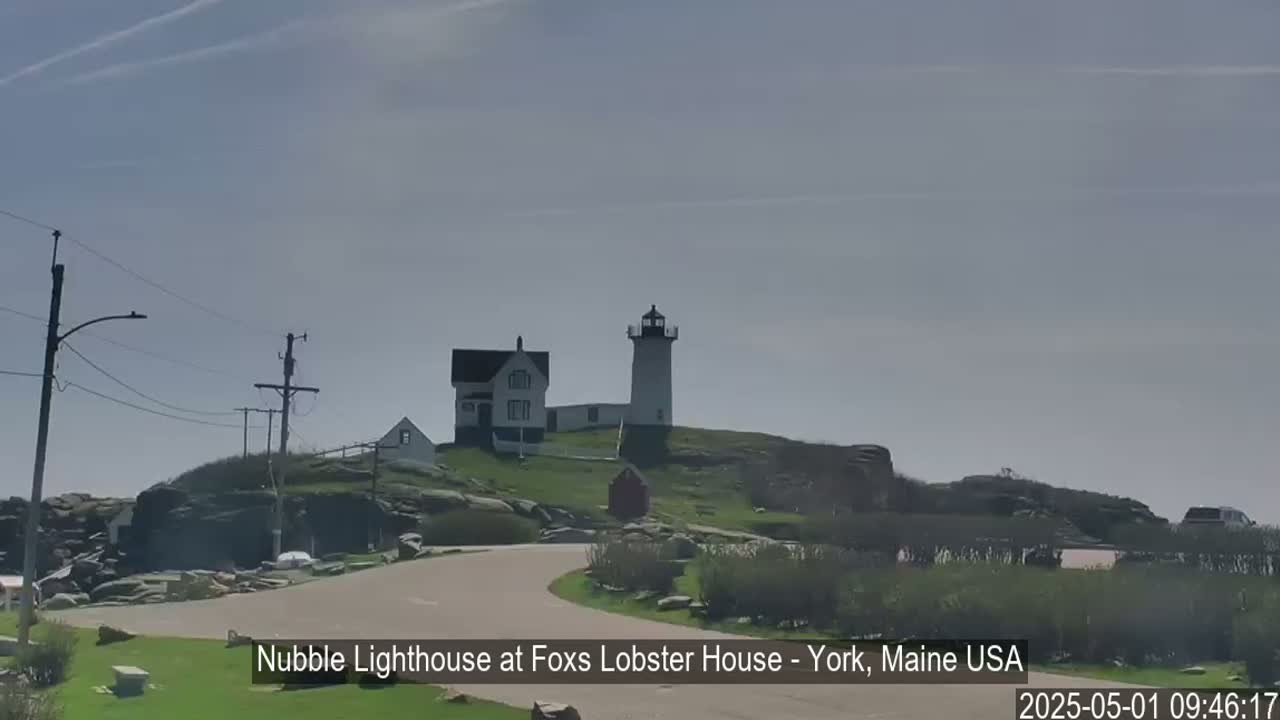 A lighthouse and a smaller building sit atop a rocky hill under a mostly clear sky.