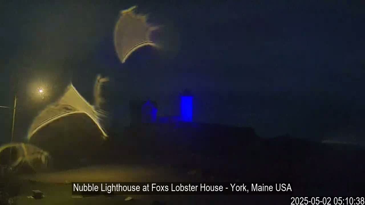 A nighttime, blurry view of a lighthouse, illuminated in blue, with what appears to be motion blur in the foreground.