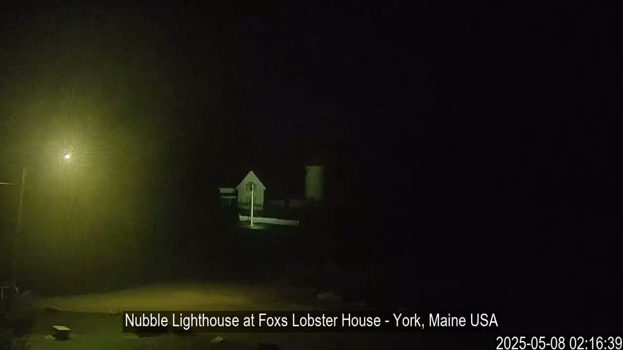 A lighthouse and a small building are dimly visible in the foggy darkness at night.