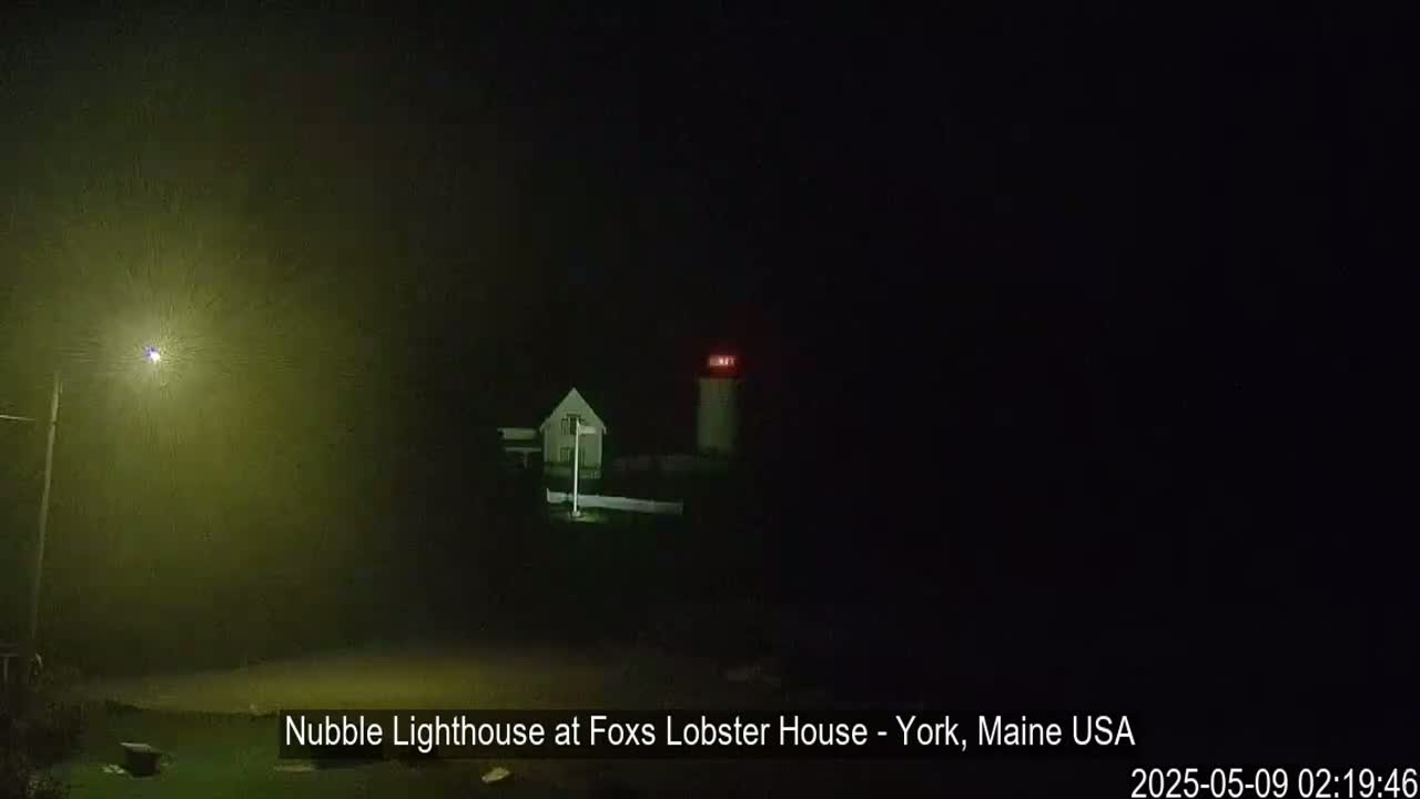 A lighthouse with a small building next to it is visible in the foggy darkness at night.
