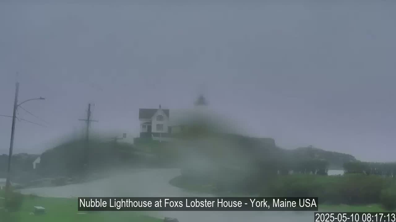 A lighthouse and a house are barely visible through heavy fog and rain.