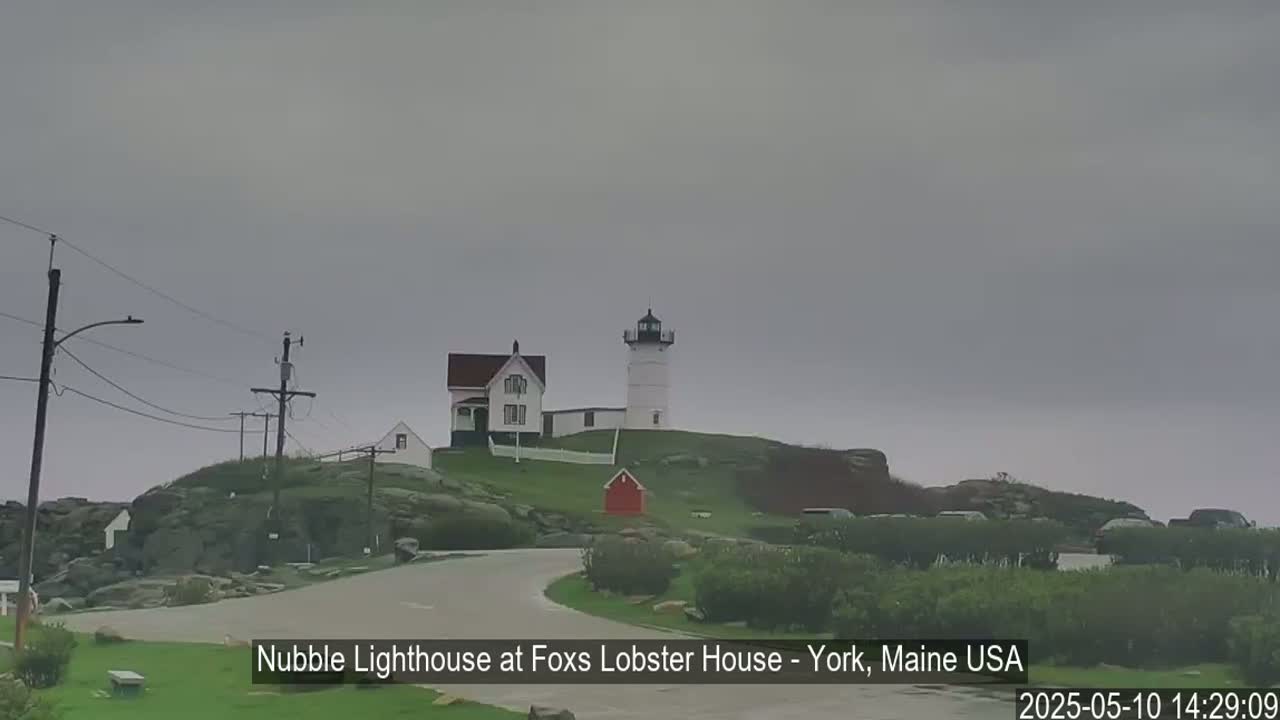 A lighthouse and accompanying buildings sit atop a rocky hill under an overcast sky.