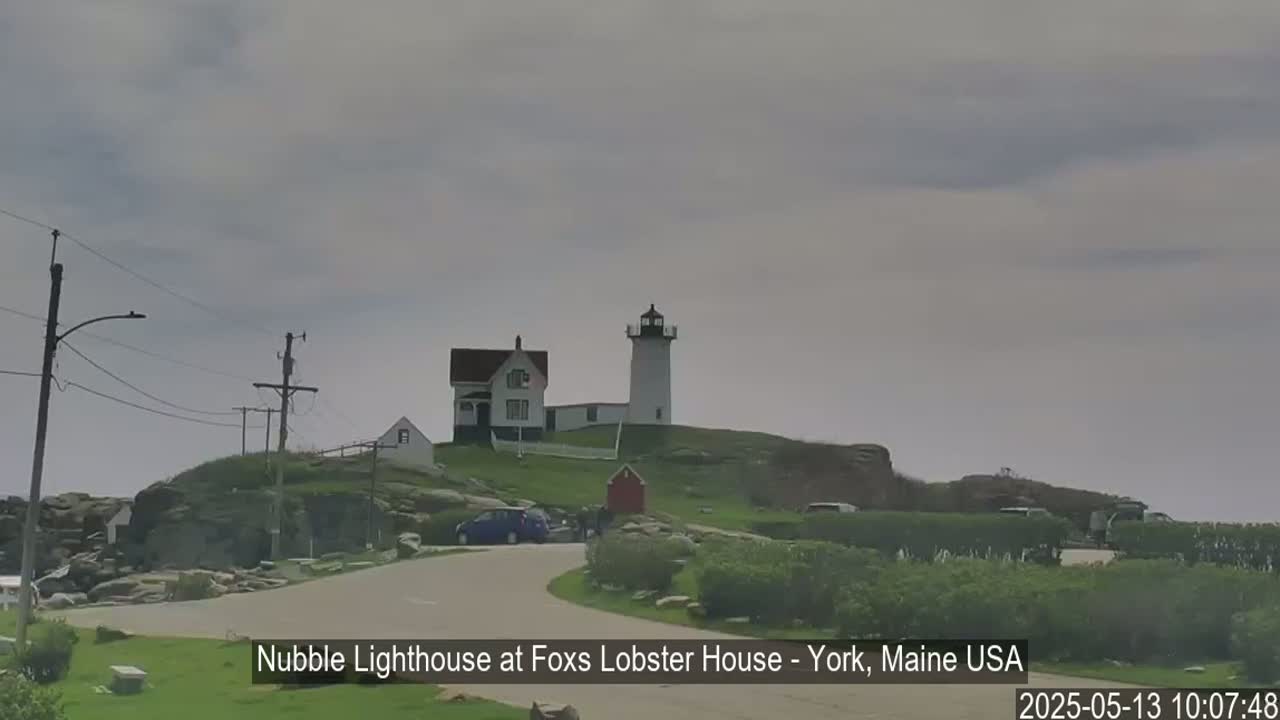 A lighthouse and adjacent buildings sit atop a rocky hill under an overcast sky.