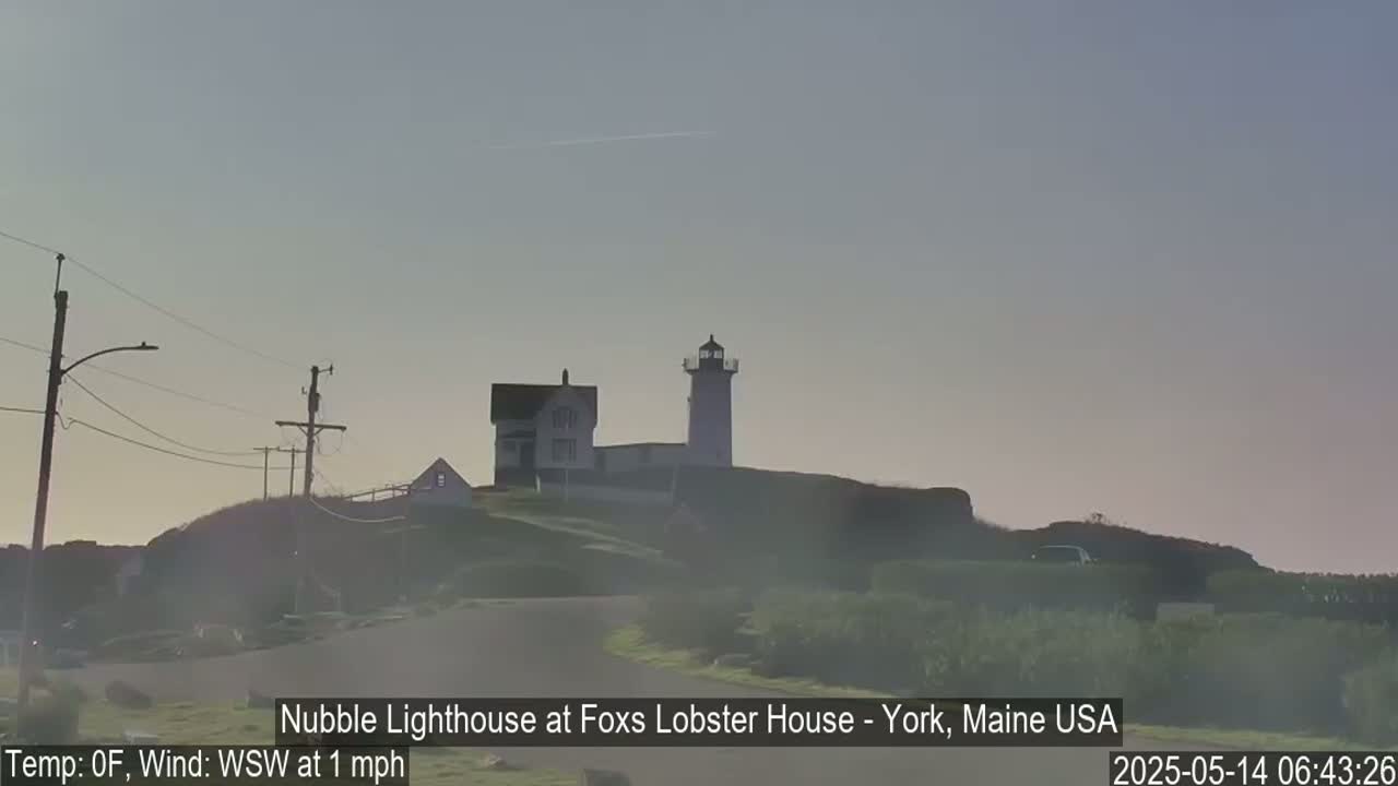 A lighthouse and adjacent building sit atop a hill on a hazy, cold morning with a light wind.