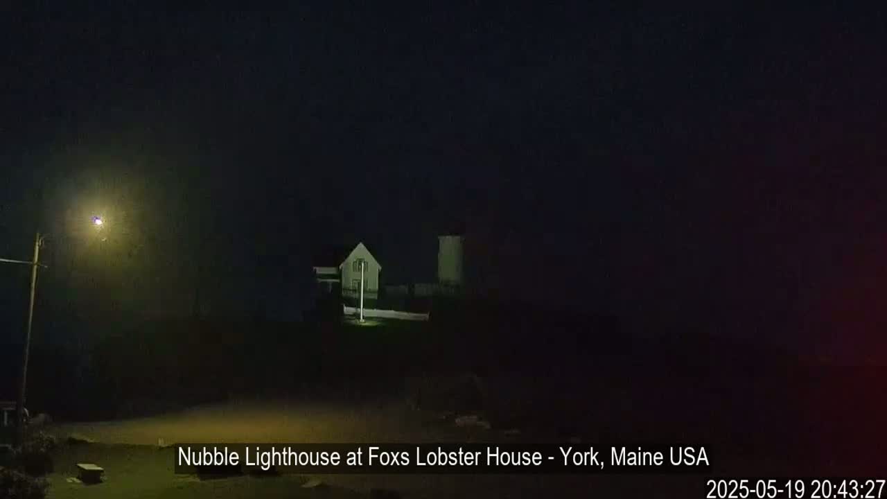 A lighthouse is dimly visible at night in foggy conditions.