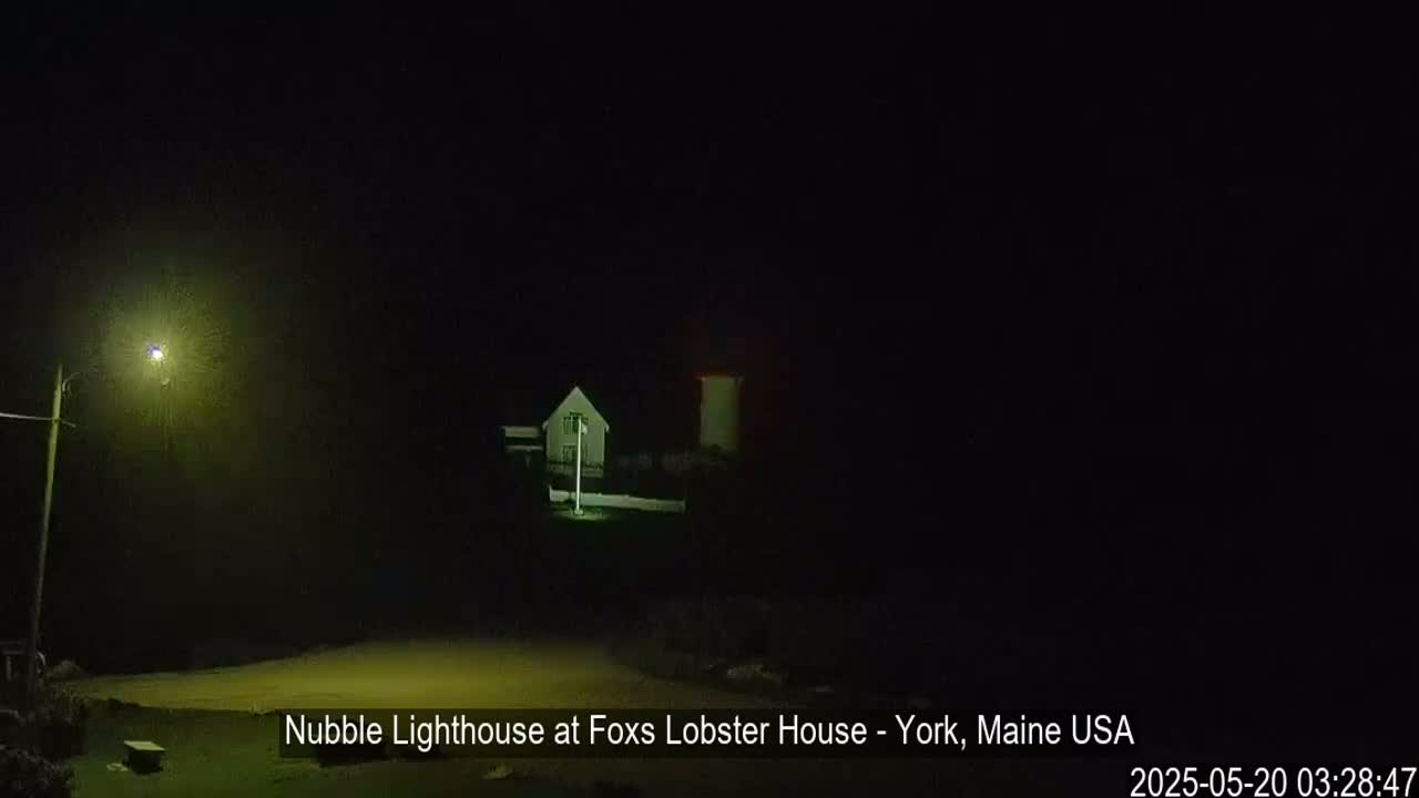 A lighthouse and a small house are visible at night, illuminated by a single streetlight.