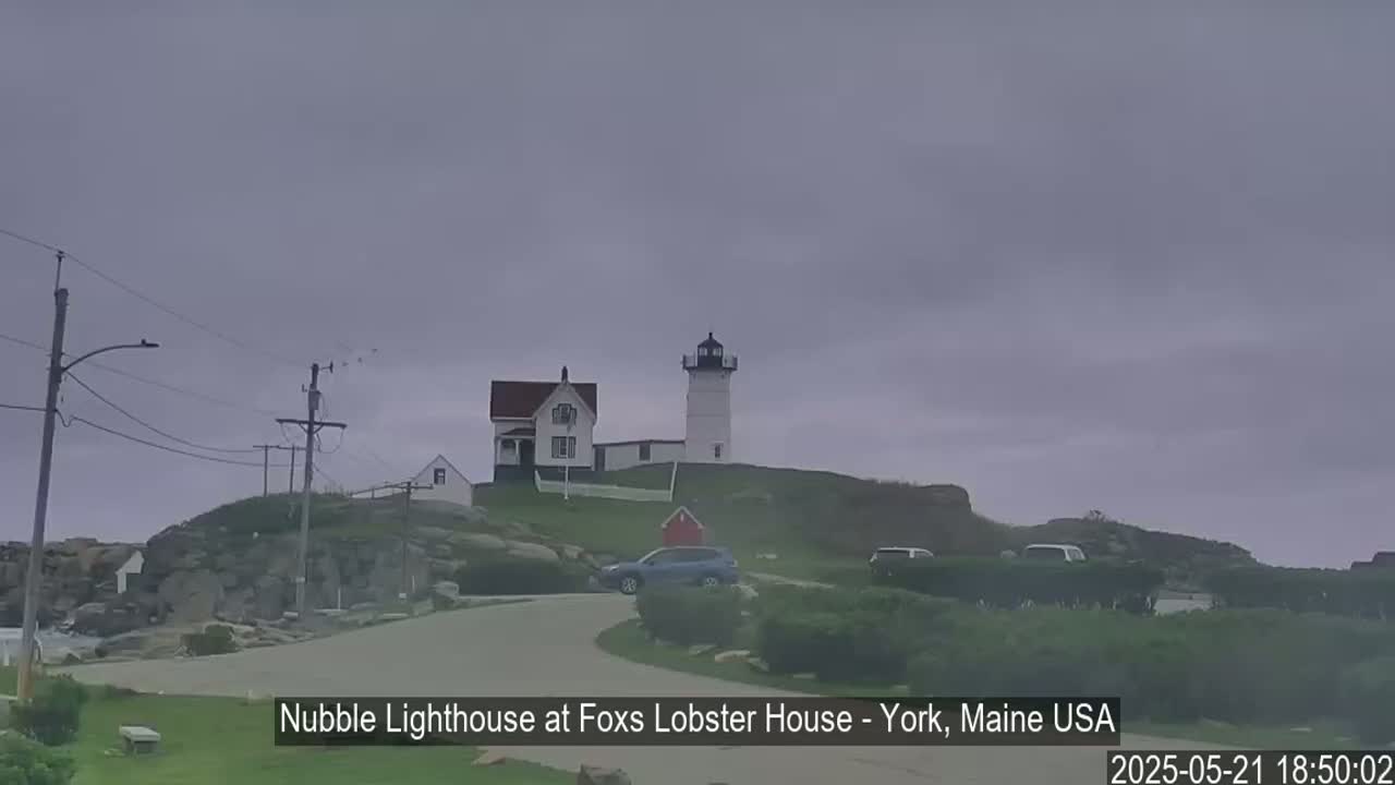 A lighthouse and keeper's house sit atop a rocky hill under an overcast sky.
