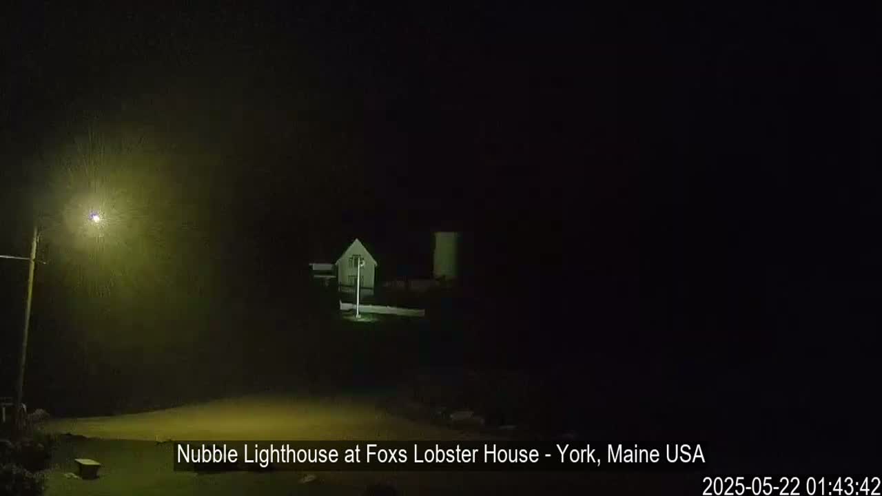 A dimly lit lighthouse and nearby building are visible through a hazy, nighttime atmosphere.