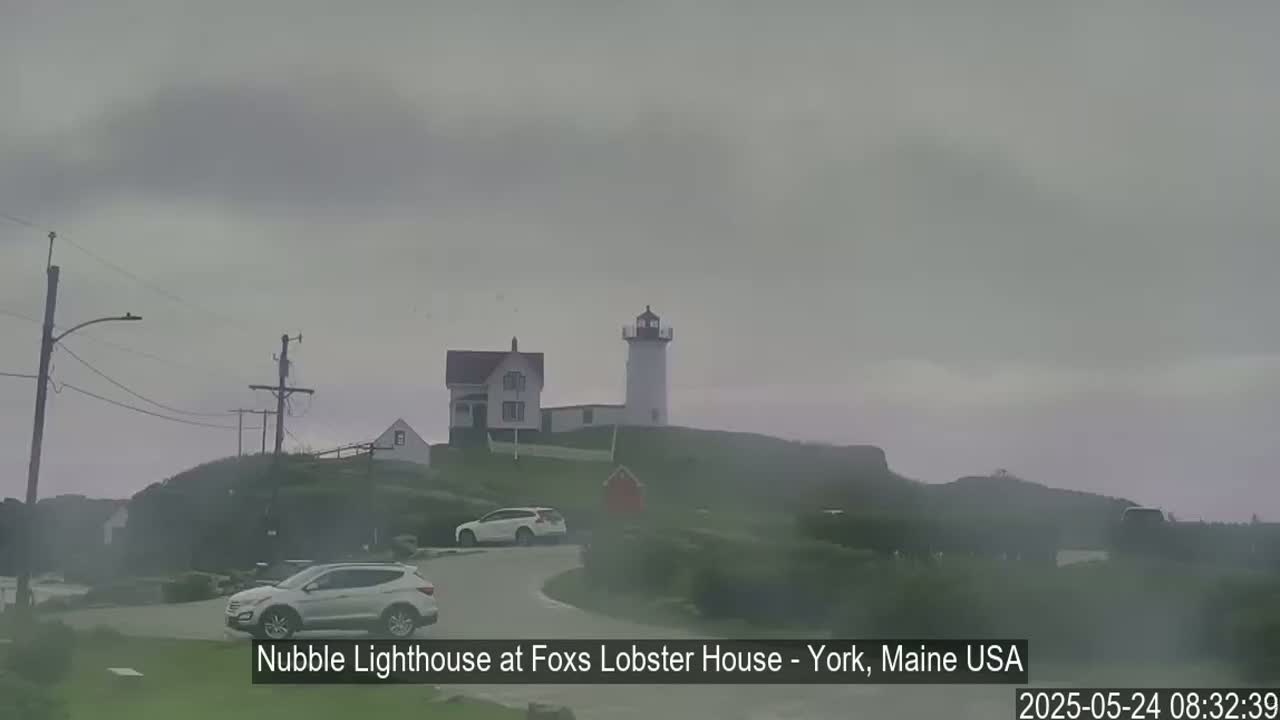 A lighthouse and several cars are visible on a foggy, overcast day.