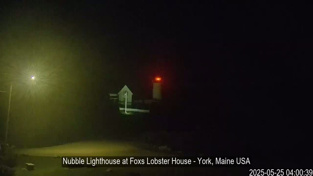 A lighthouse with a red light is visible at night in foggy conditions.
