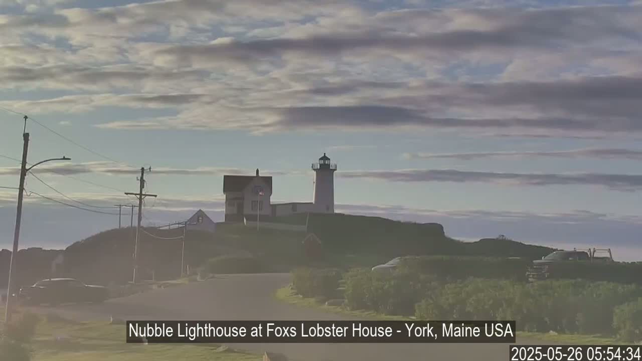 A lighthouse sits atop a small hill under a mostly cloudy sky.