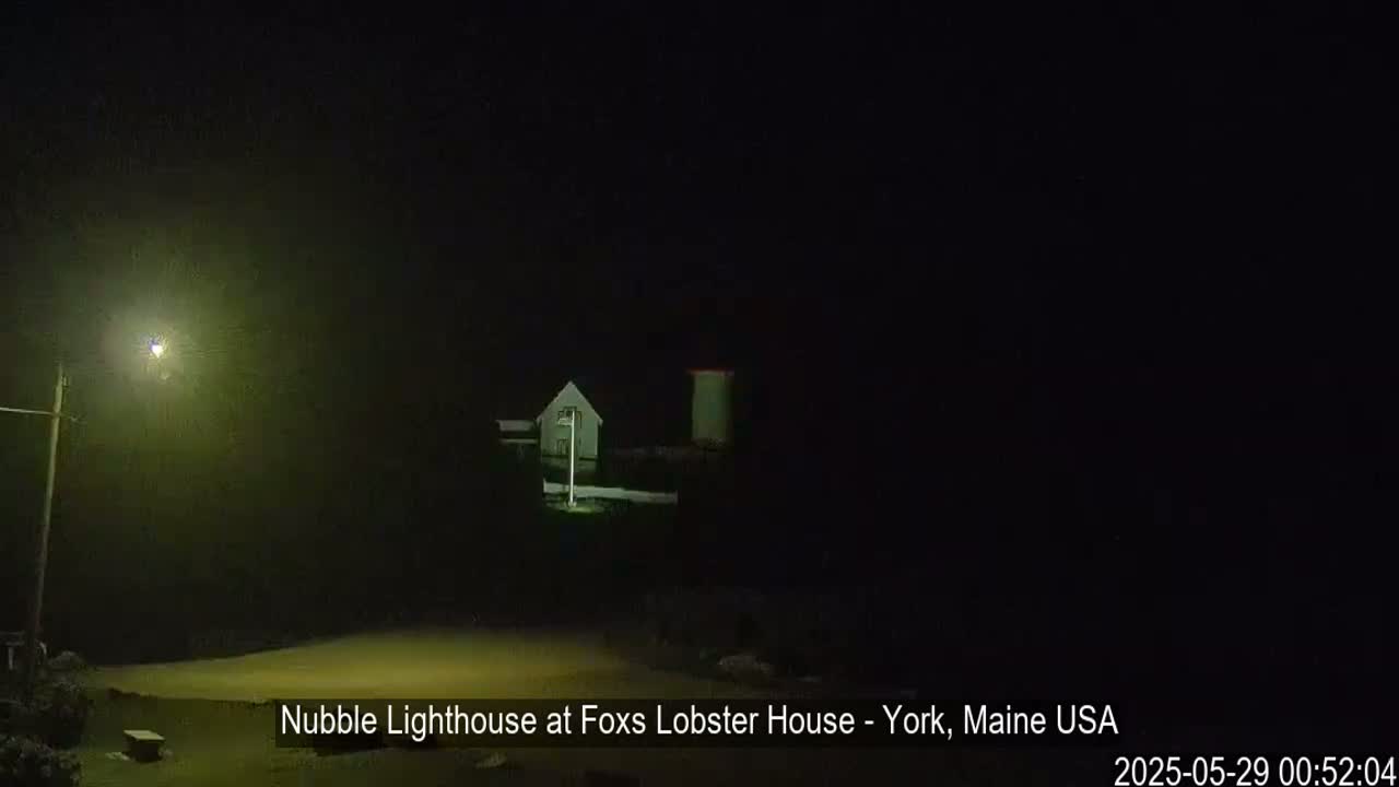 A lighthouse and a building are dimly lit at night in foggy conditions.