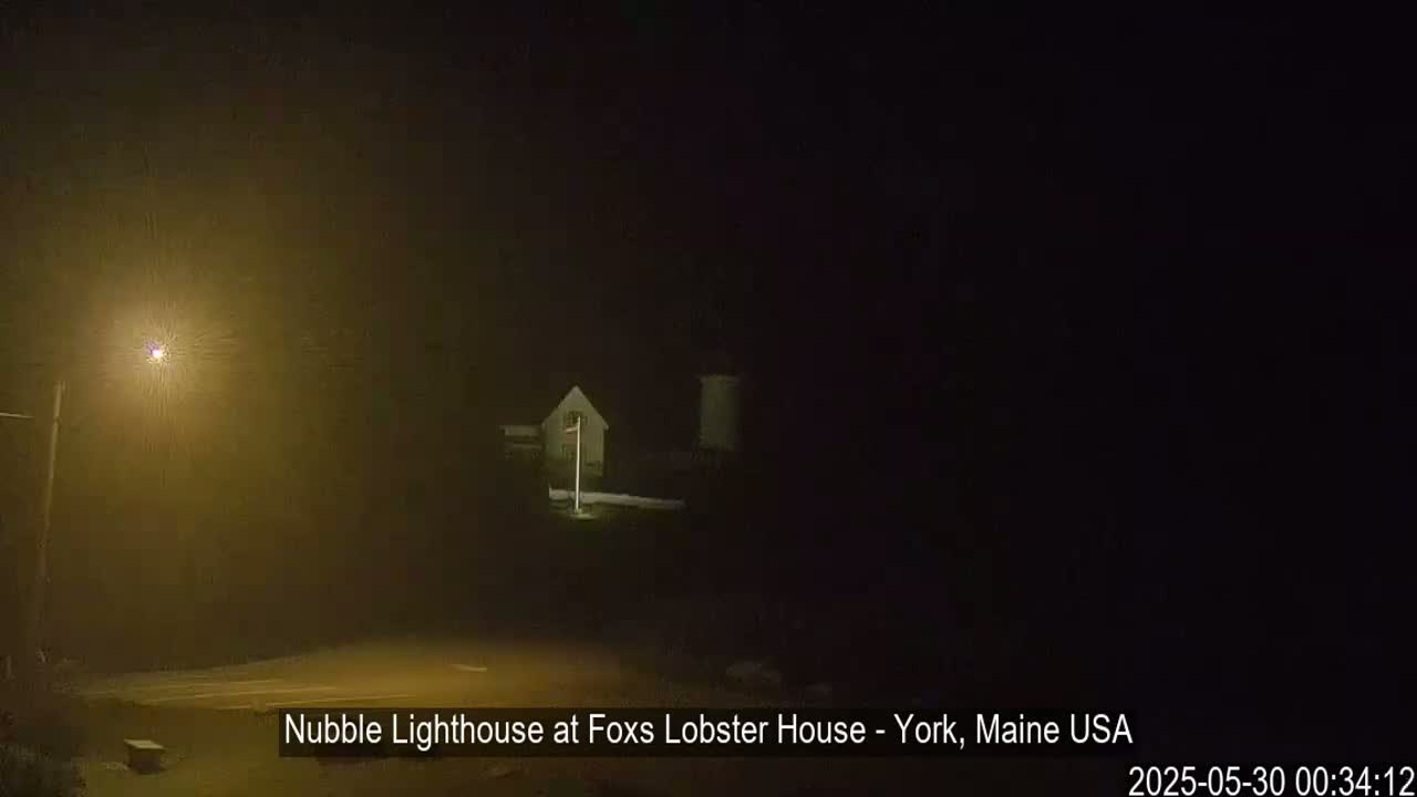 A dimly lit lighthouse is visible through heavy fog at night.