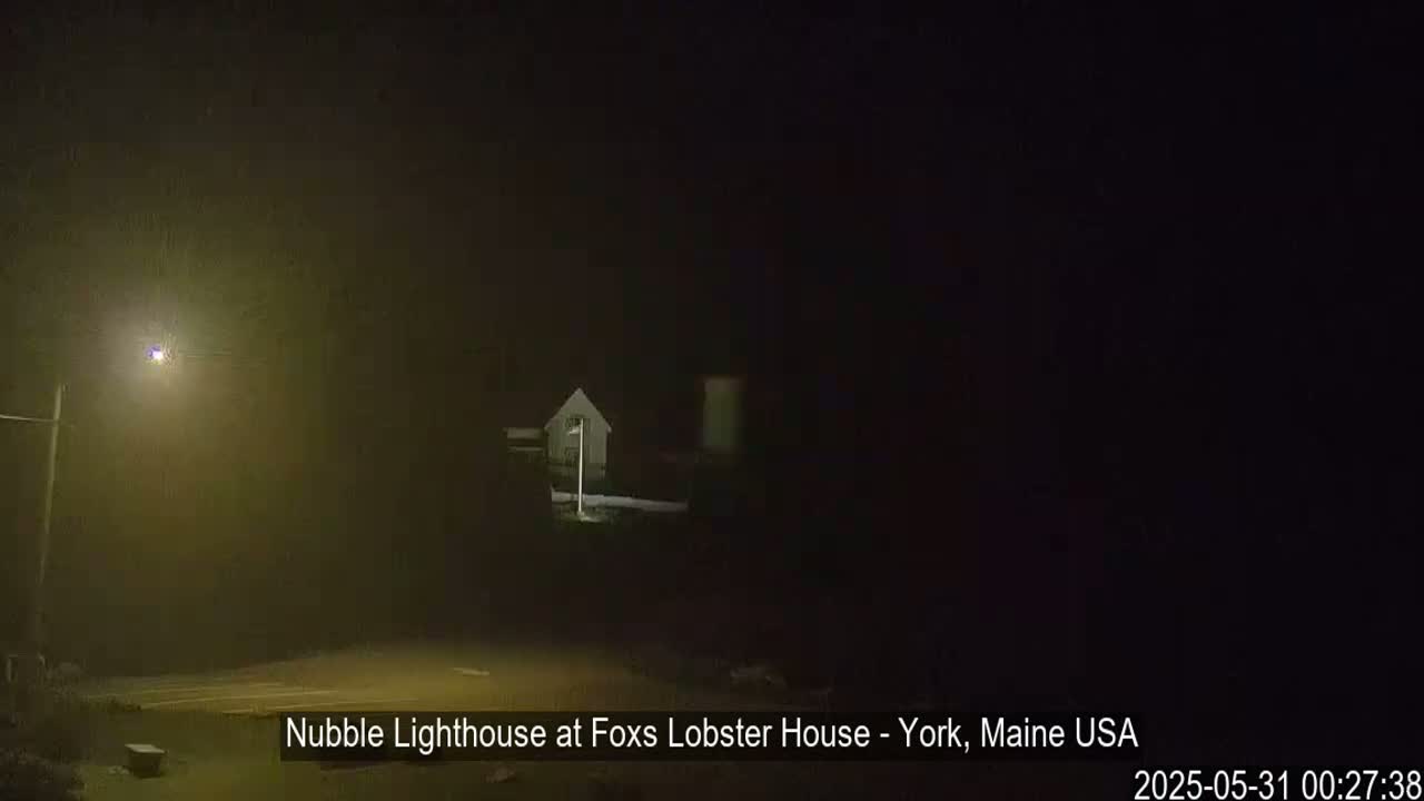 A dimly lit lighthouse is visible through heavy fog at night.
