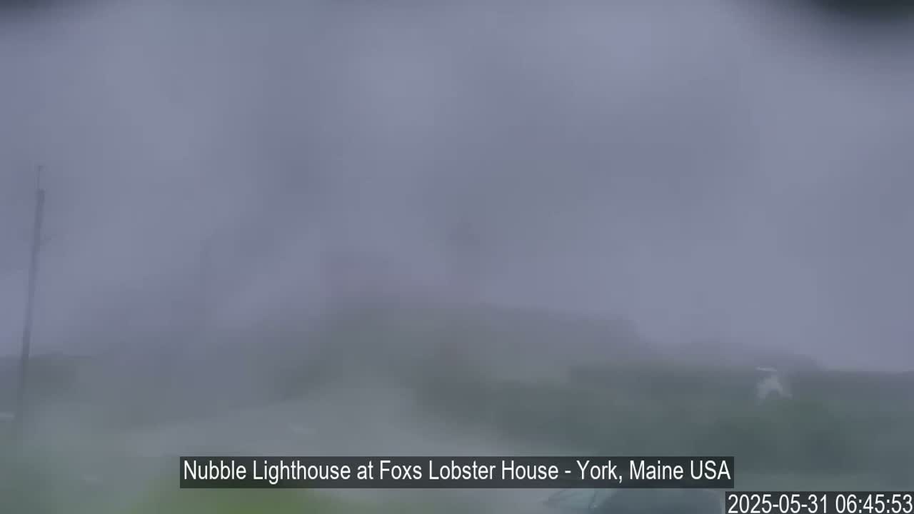 A blurry view of a foggy coastal scene shows a lighthouse barely visible through heavy mist.