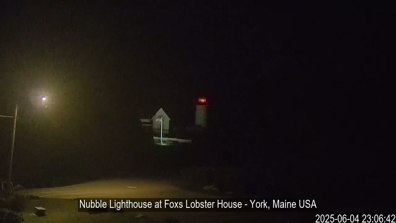 A lighthouse with a red light shines at night in dark, unclear weather conditions.