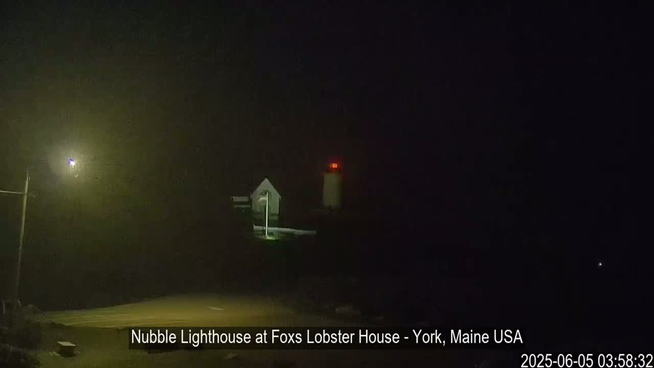 A lighthouse with a small building nearby is visible at night in foggy conditions.