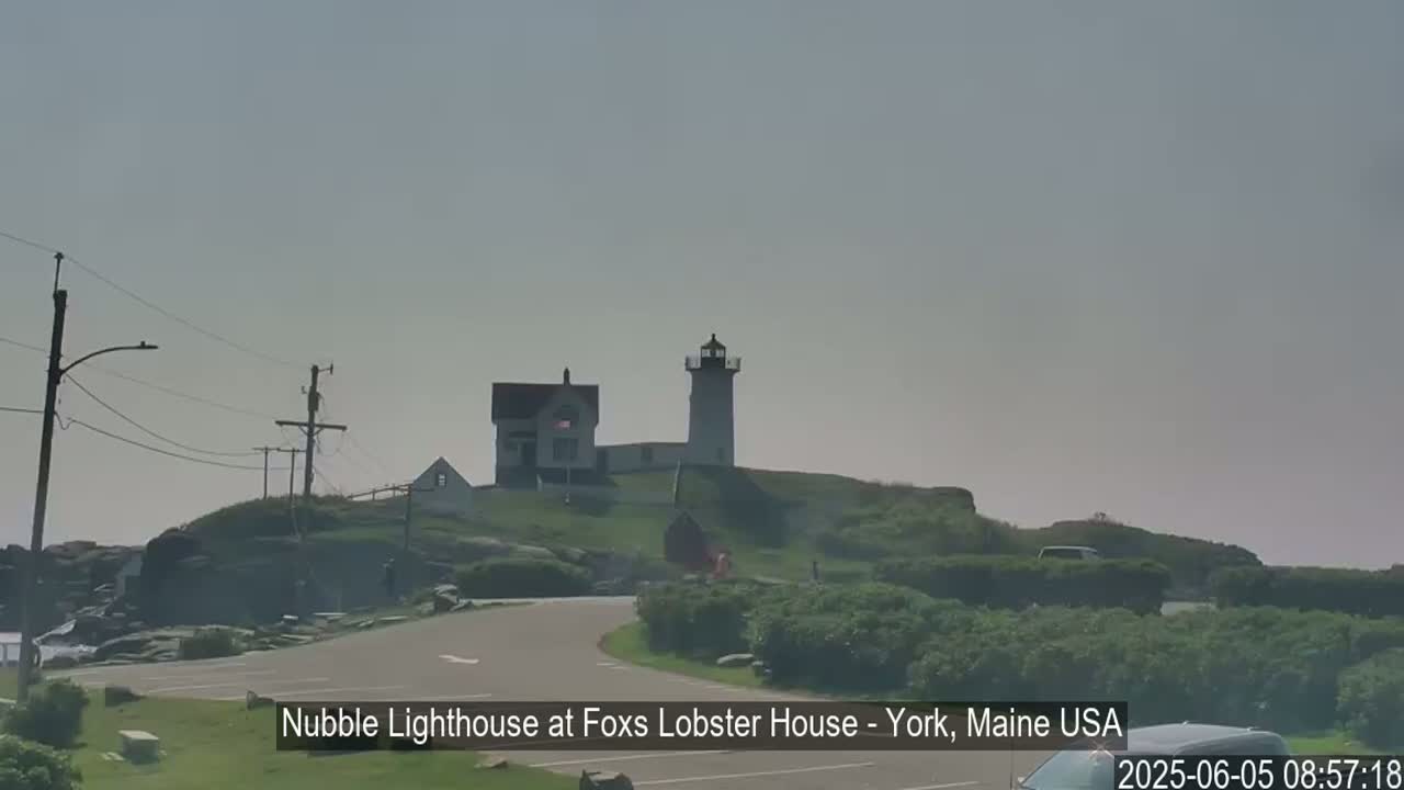 A lighthouse and keeper's house sit atop a rocky hill on a hazy day.