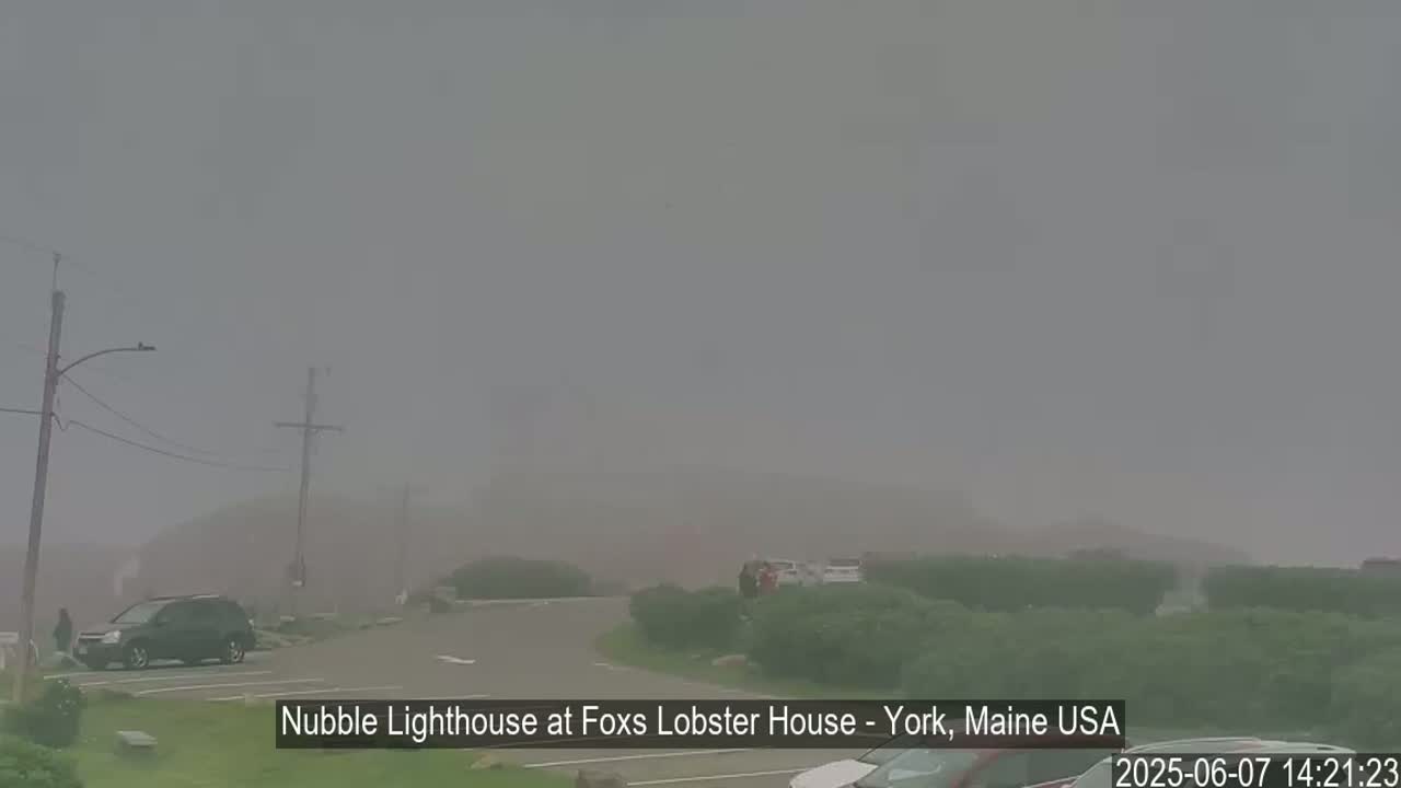 A foggy parking lot with a few cars and some shrubbery is visible, with a lighthouse barely seen in the distance.