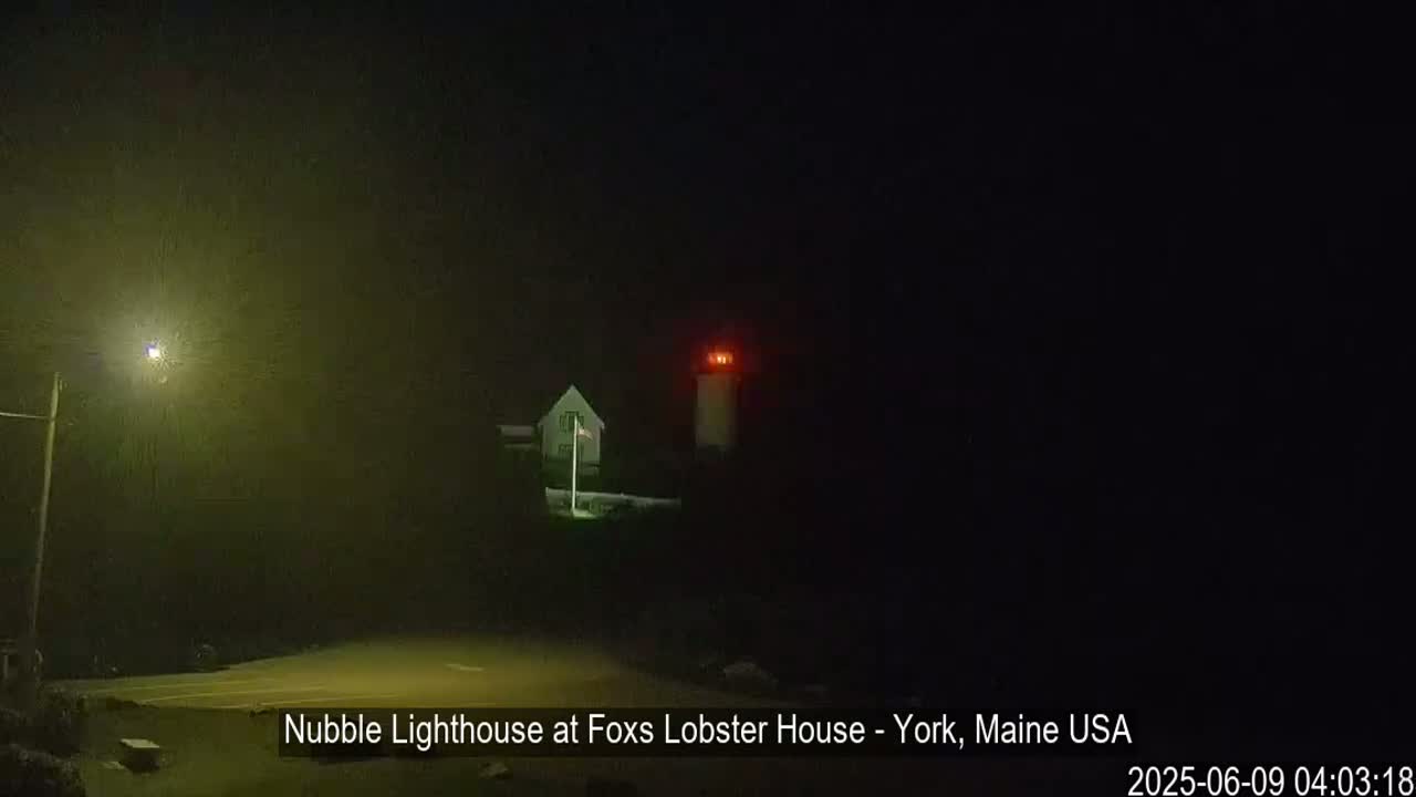 A lighthouse with a red light atop it is visible at night in foggy conditions.