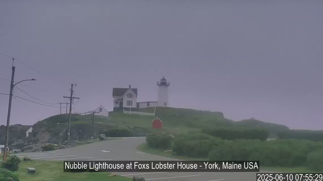 A lighthouse and a smaller building sit atop a grassy hill on a foggy day.