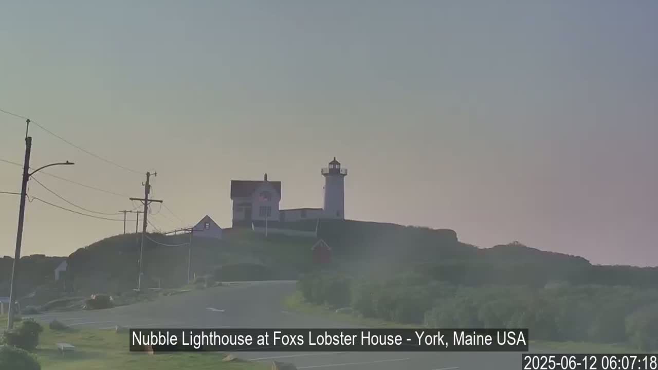 A lighthouse and accompanying buildings sit atop a hill on an overcast morning.