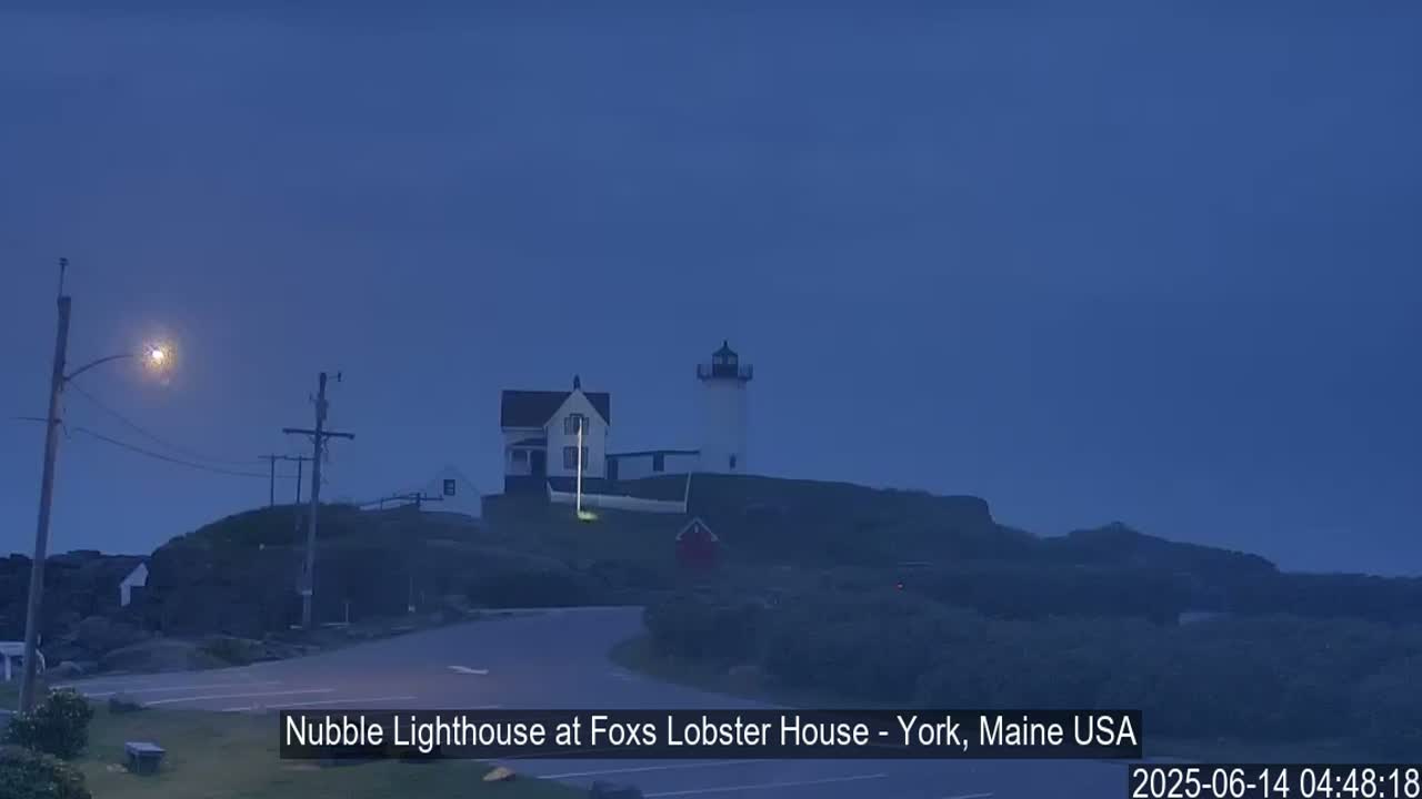 A lighthouse and adjacent building are situated on a dark, rocky hill under a twilight sky.