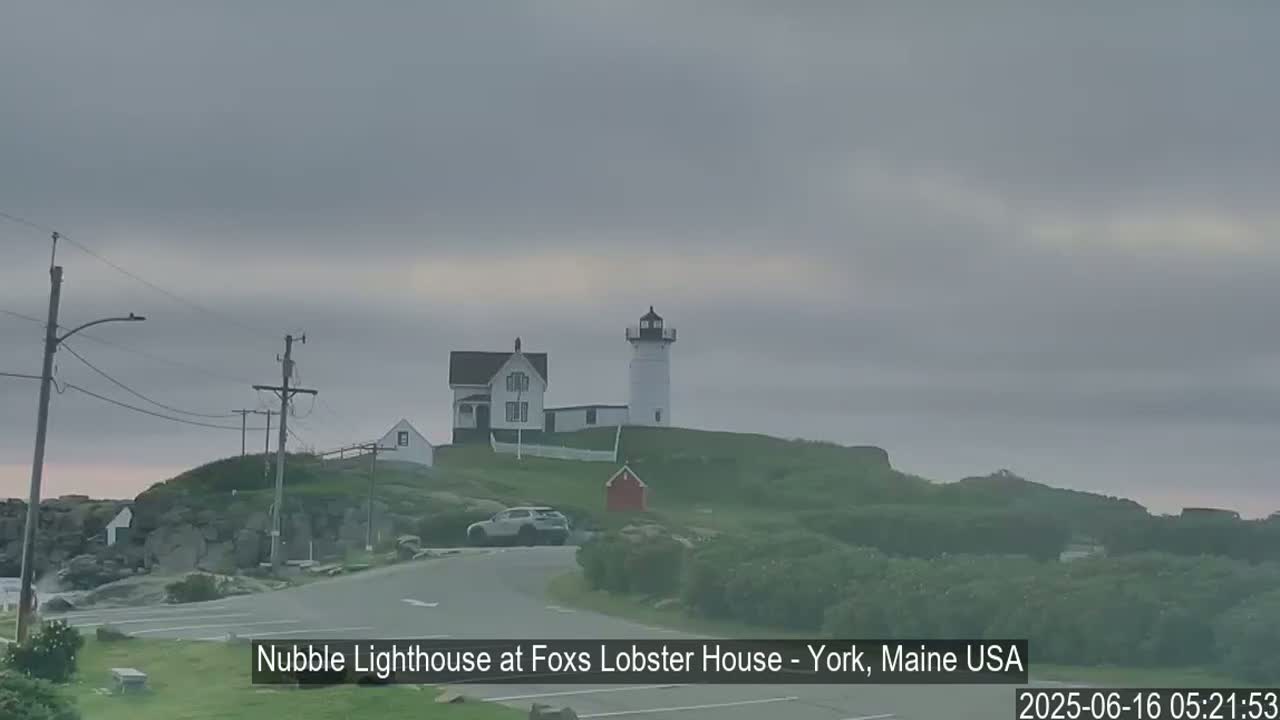A lighthouse and keeper's house sit on a rocky hill under an overcast sky.