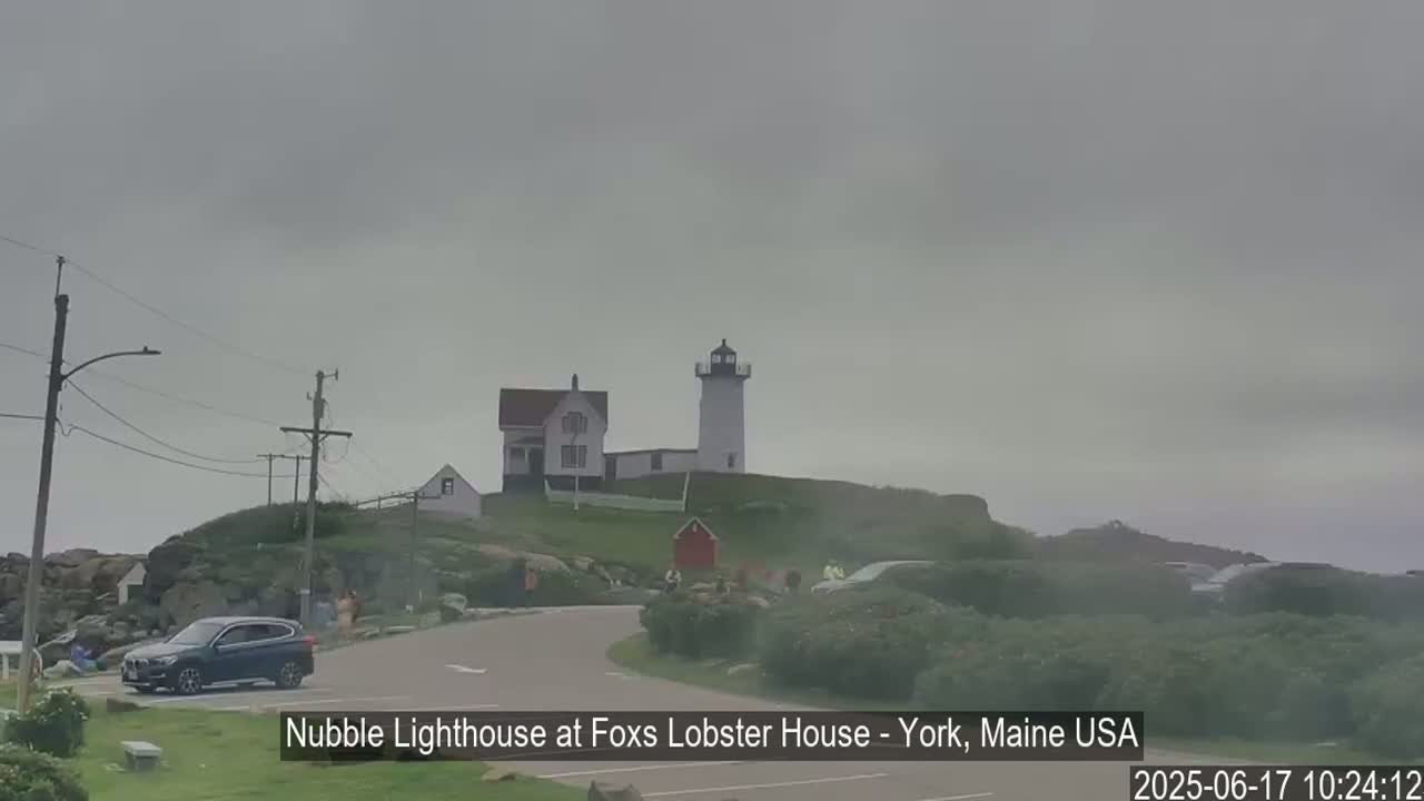 A lighthouse and accompanying buildings are situated on a rocky coast under an overcast sky.