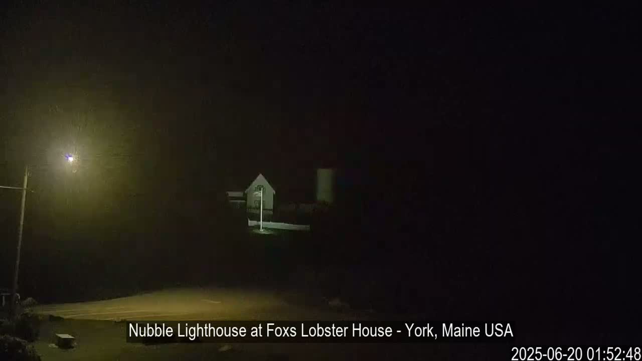 A lighthouse is dimly visible in the foggy darkness, illuminated by a streetlight.
