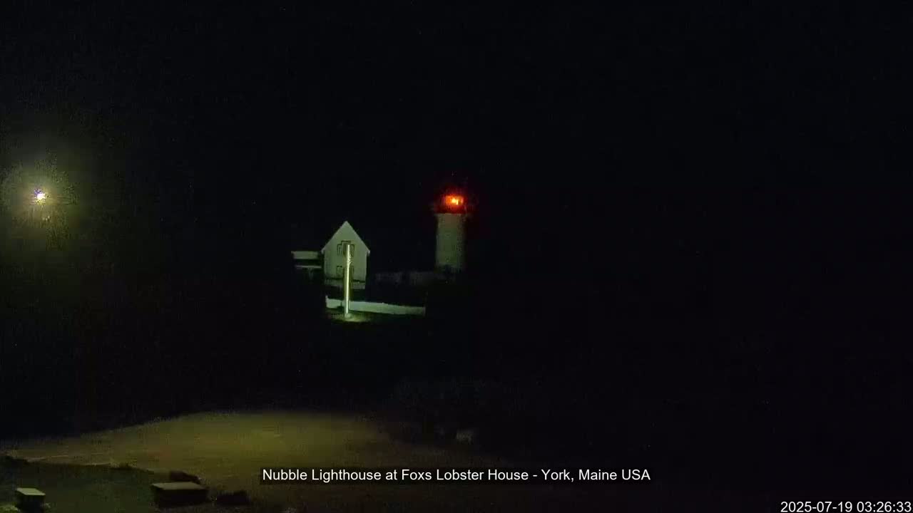 A lighthouse with a red light at its top is visible at night, next to a smaller building.