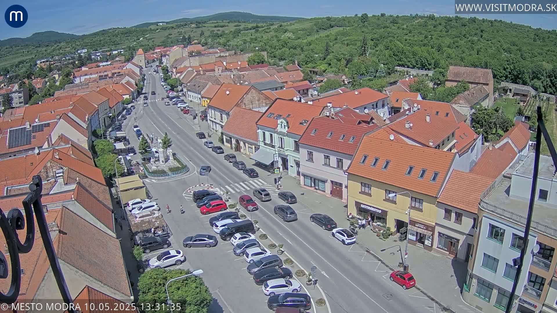 An aerial view of a town square and street lined with buildings under a sunny sky.