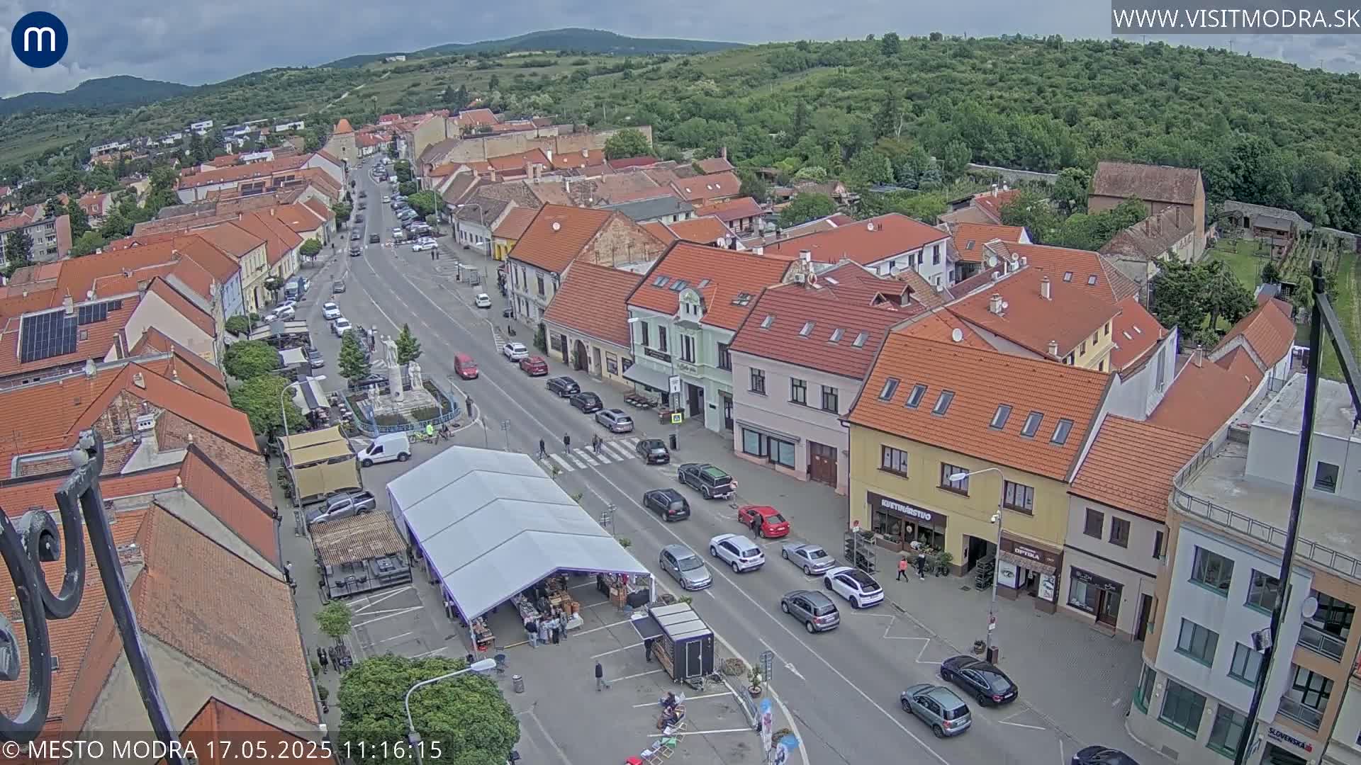 An aerial view of a town square with a street lined with buildings and cars under a partly cloudy sky.