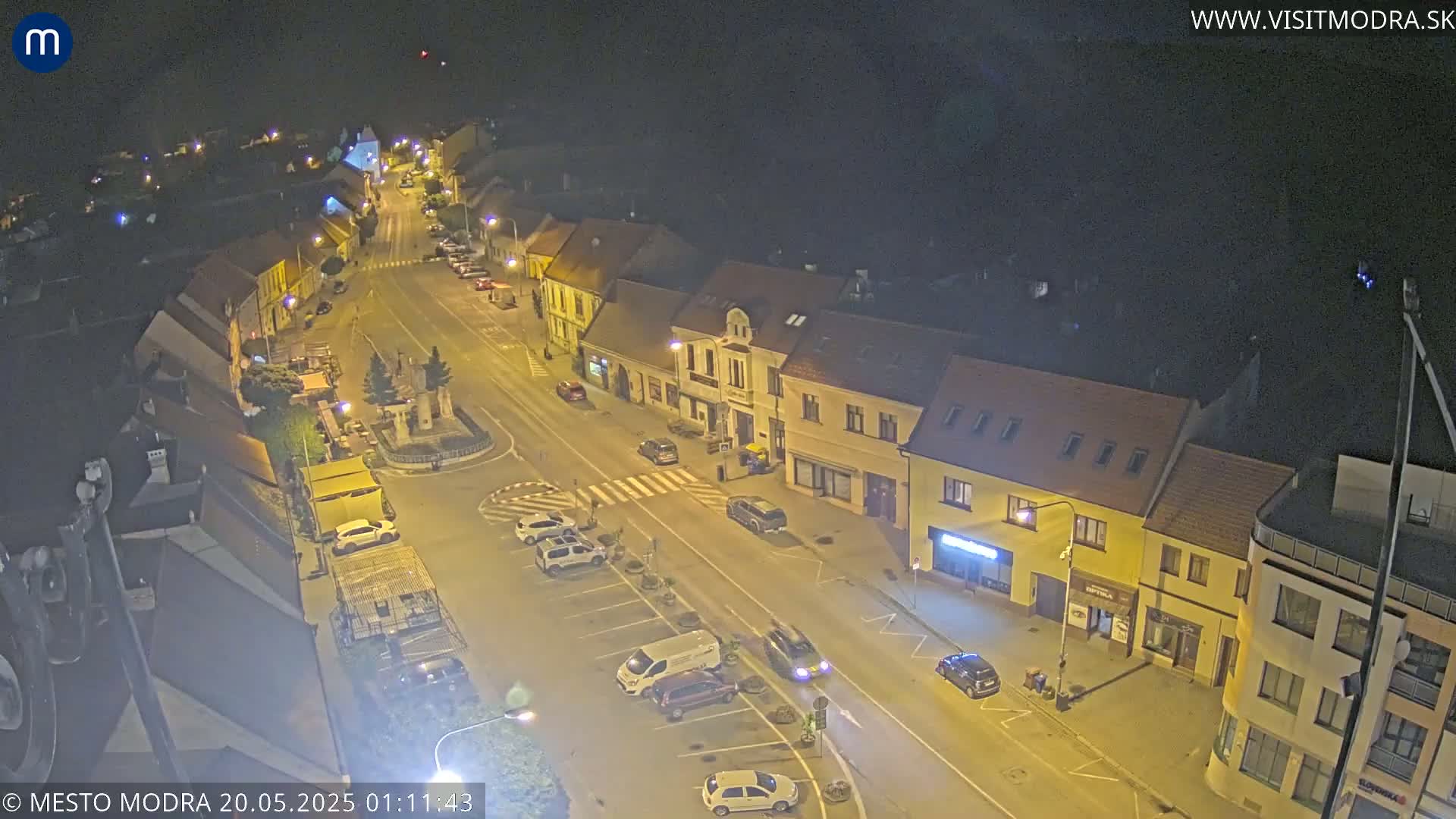 A nighttime, high-angle view of a town square and surrounding buildings, illuminated by streetlights.