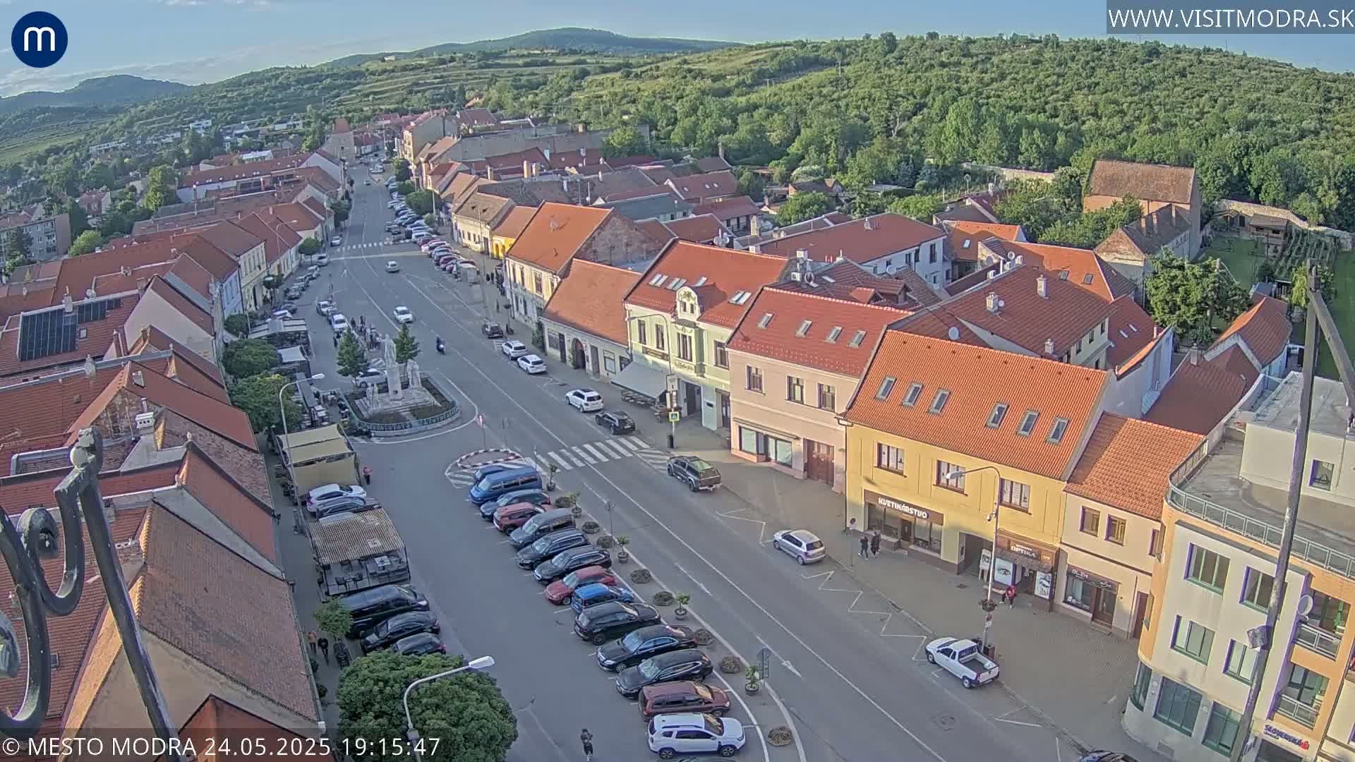 An aerial view of a town square with cars parked along the street, under a mostly clear evening sky.