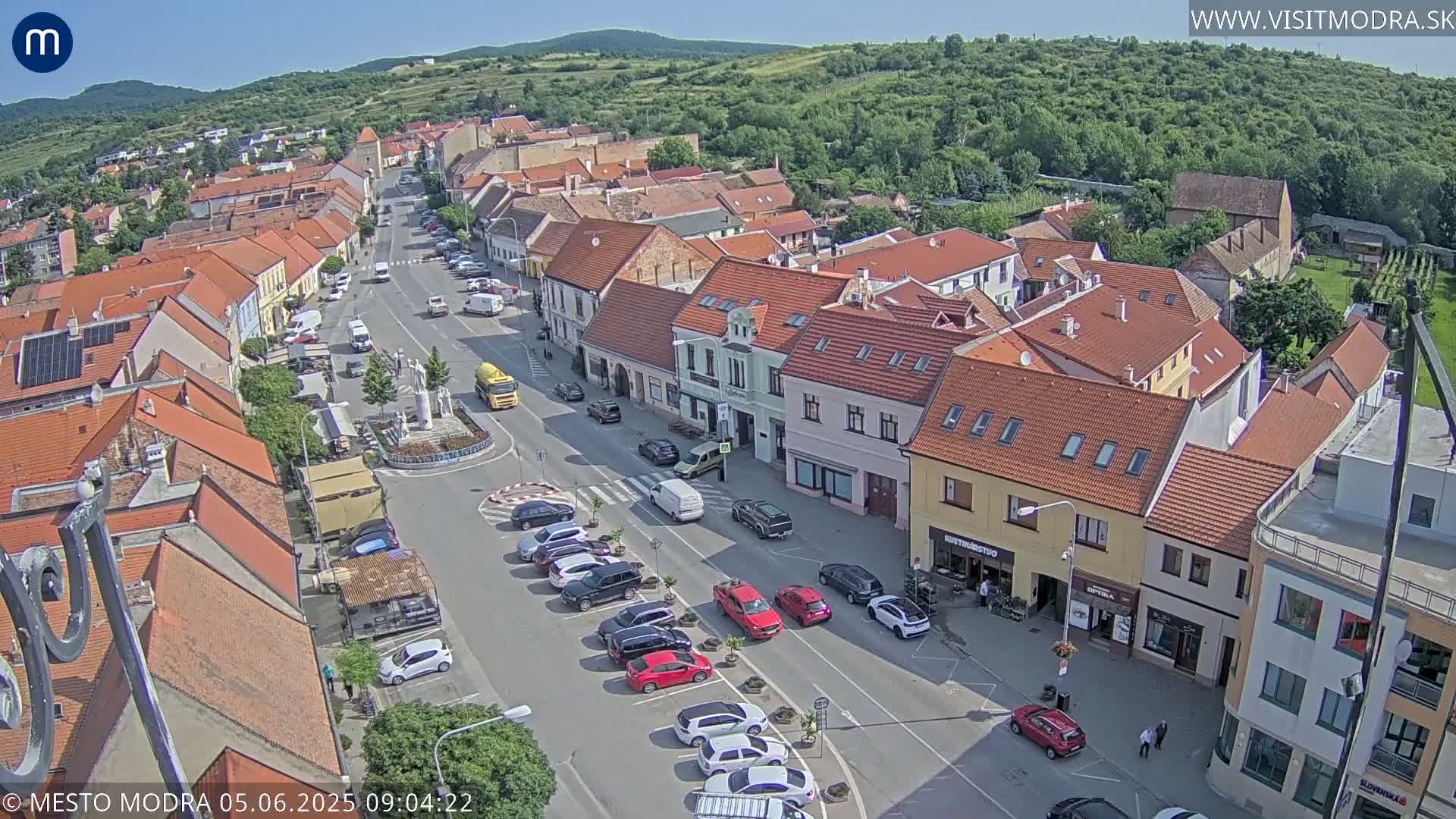 An aerial view of a town square with many parked cars and buildings under a sunny sky.