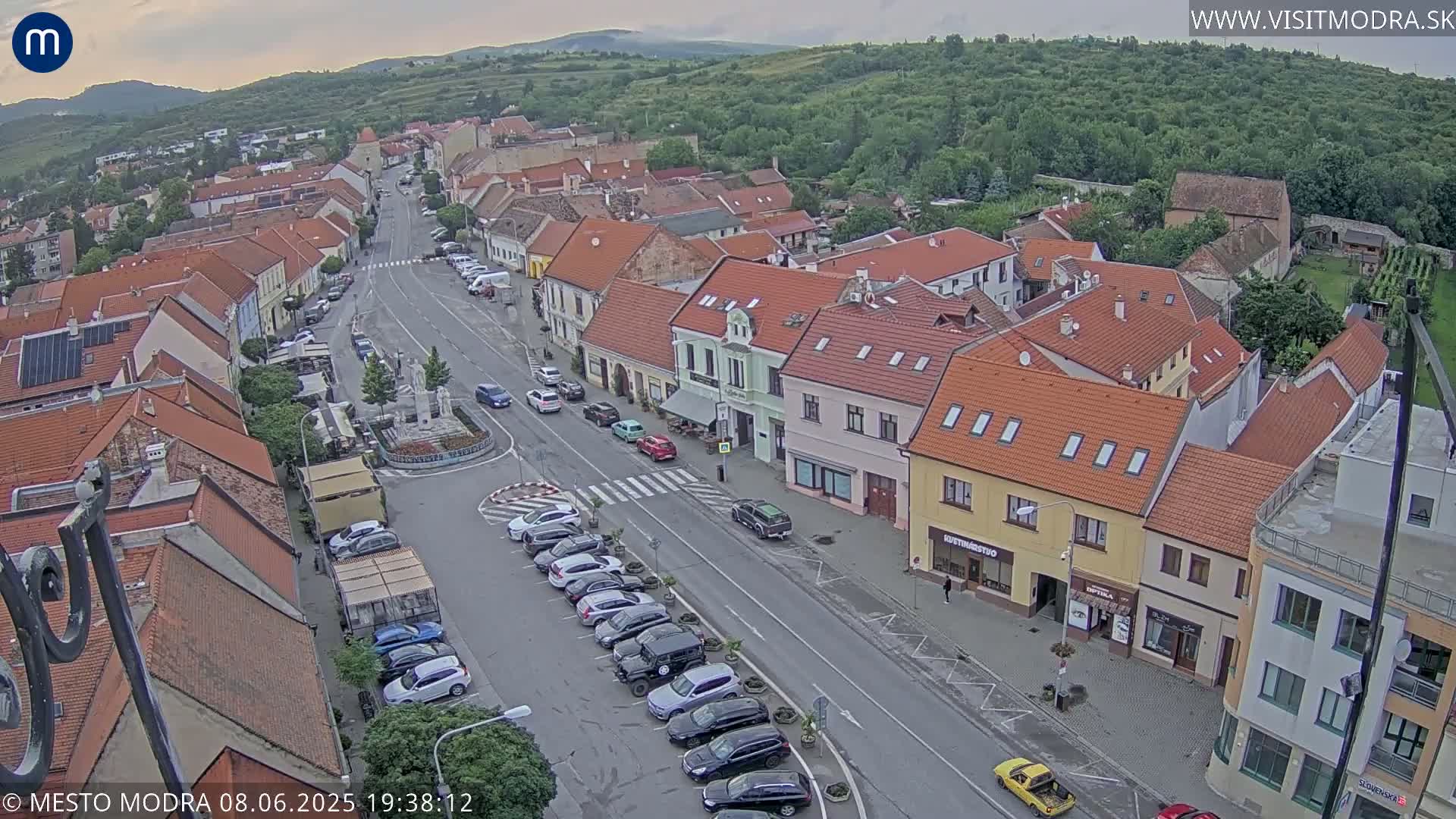 An aerial view of a town square and surrounding buildings under partly cloudy skies.