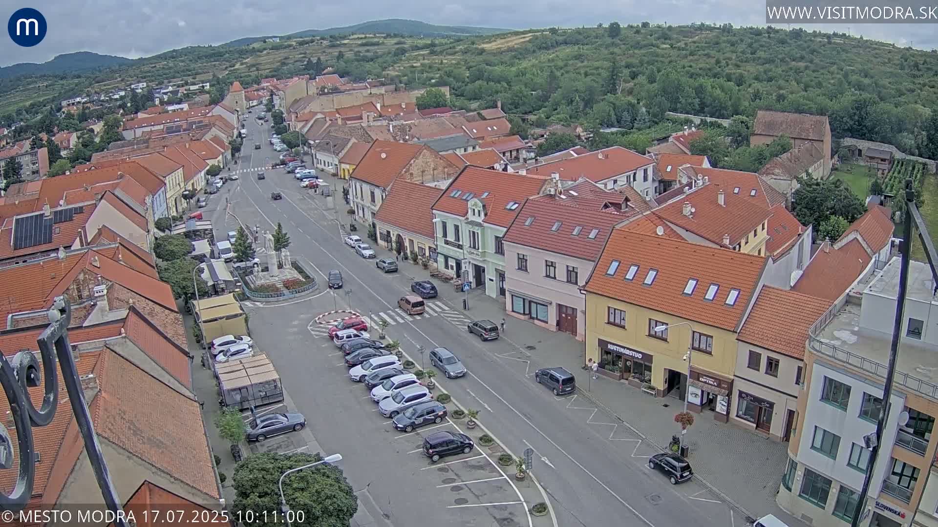 An aerial view of a town square and surrounding buildings on an overcast day, with cars parked along the streets.