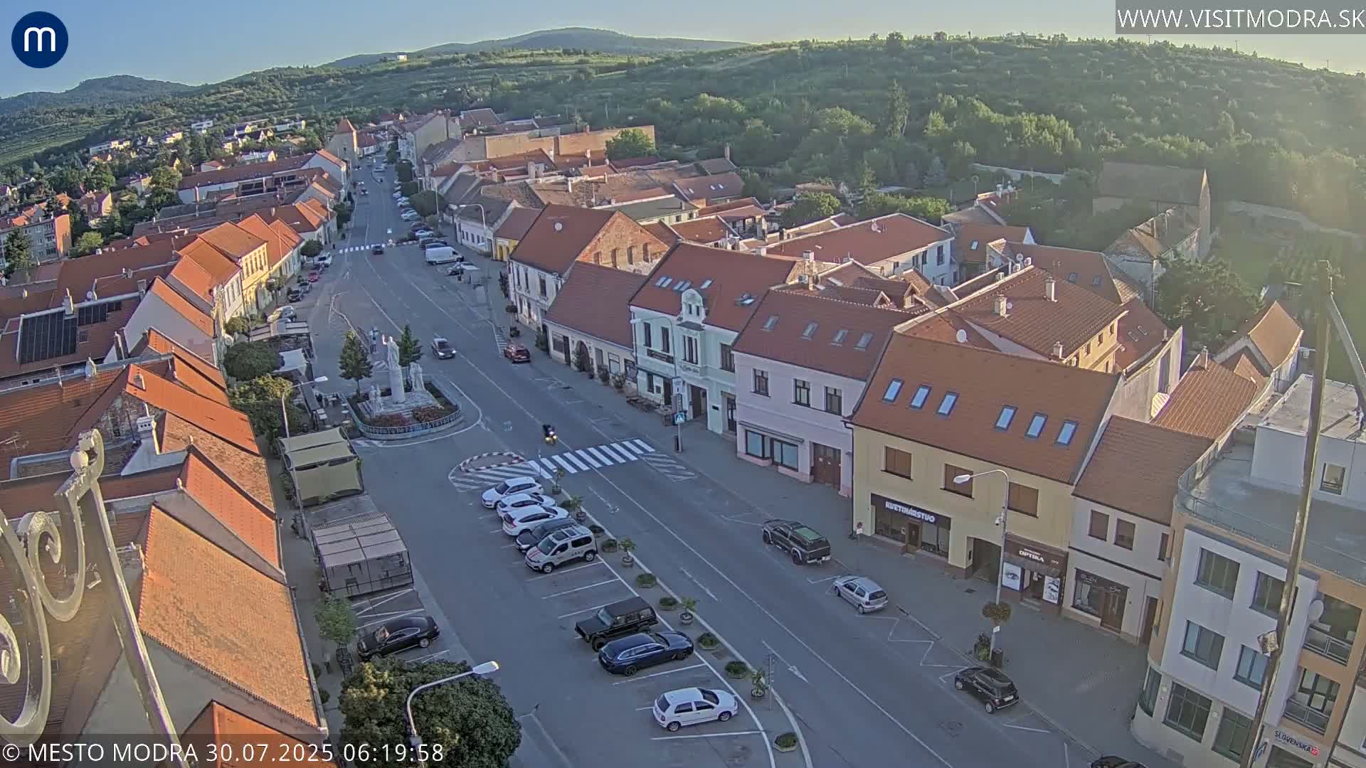 An aerial view of a town square and surrounding buildings on an overcast day, with cars parked along the streets.