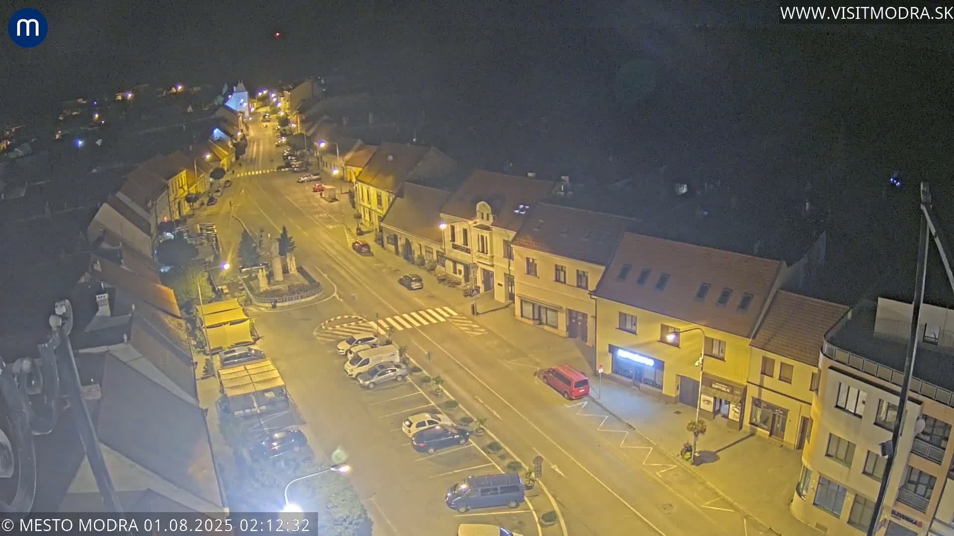 A nighttime, high-angle view of a town's street and buildings with cars parked along the sides.