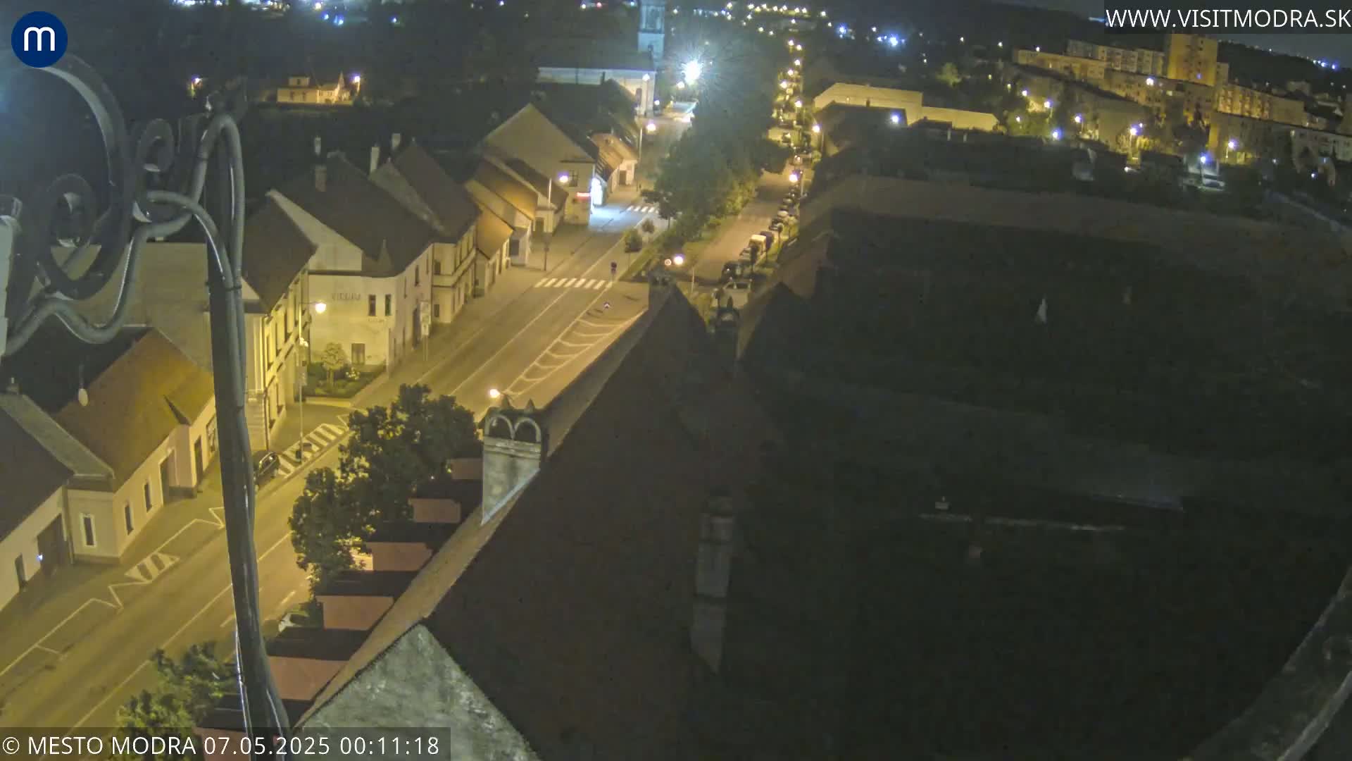 A nighttime high-angle view of a town's street and buildings, illuminated by streetlights.