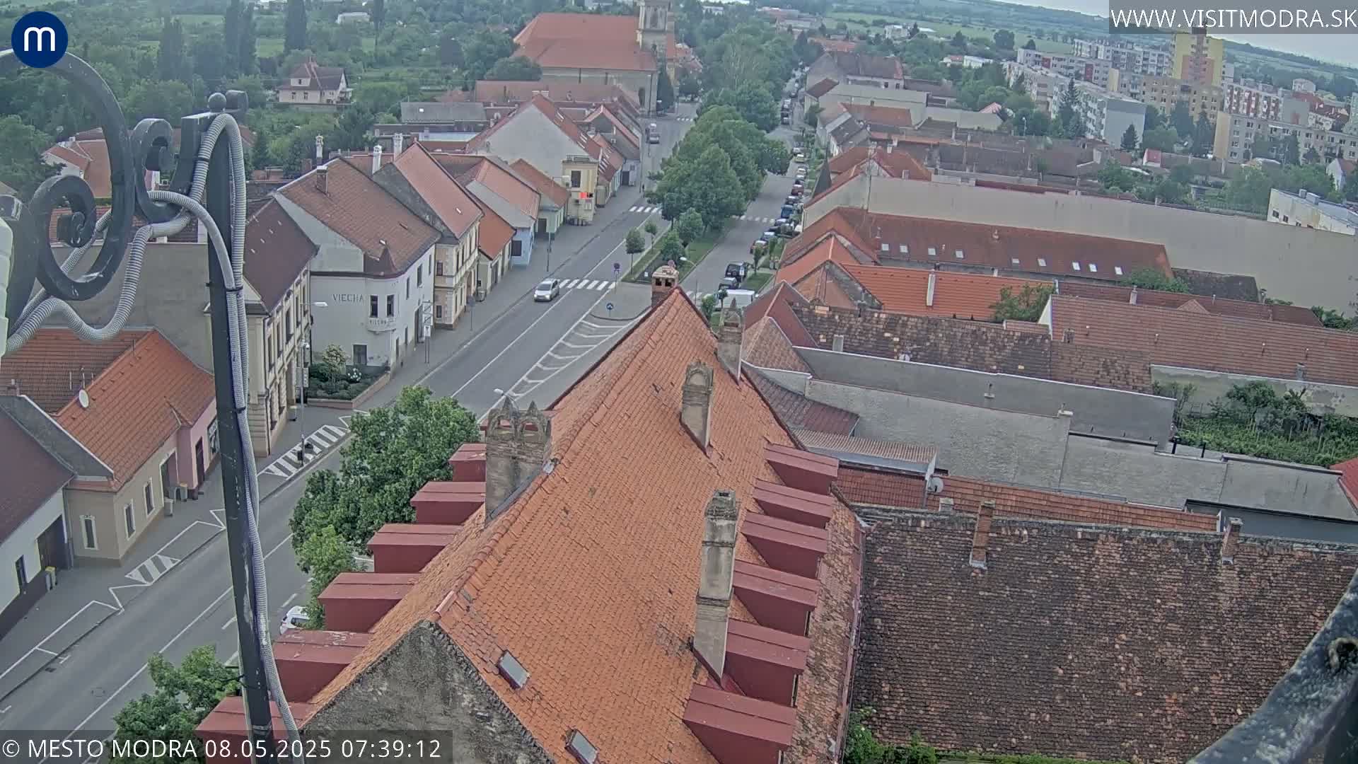 An overcast day reveals a high-angle view of a town's rooftops and streets, with a few cars visible on the road.