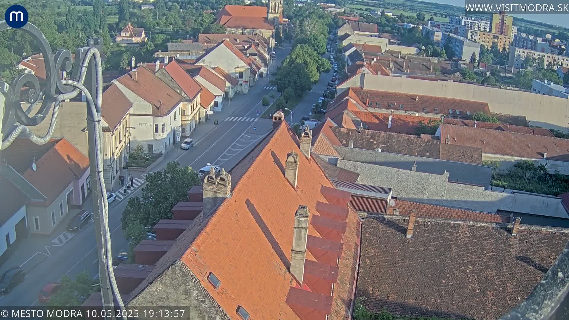An aerial view of a town's red-tiled rooftops and streets on a sunny day.