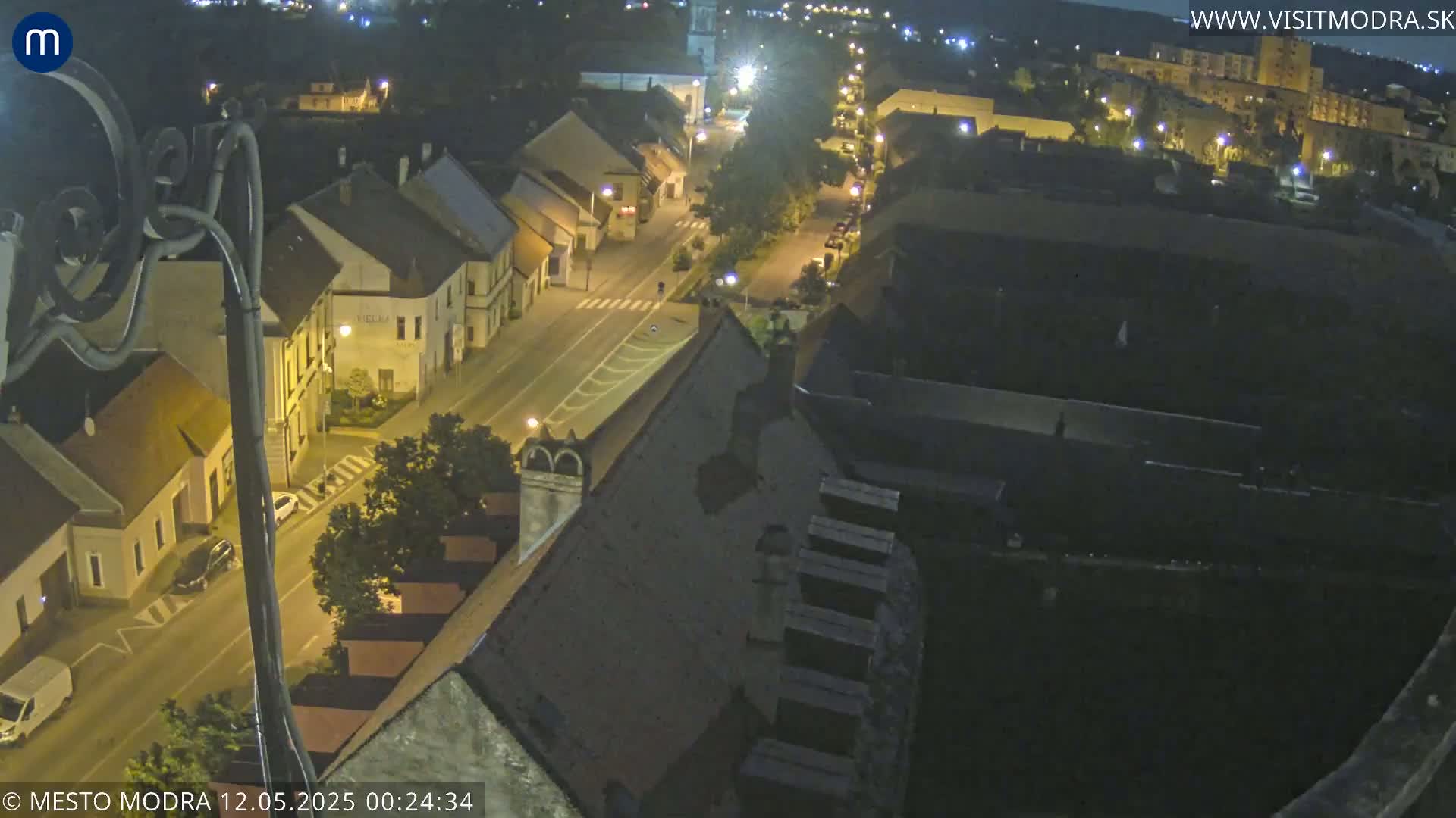 A nighttime, high-angle view shows a street in a town with buildings illuminated by streetlights.